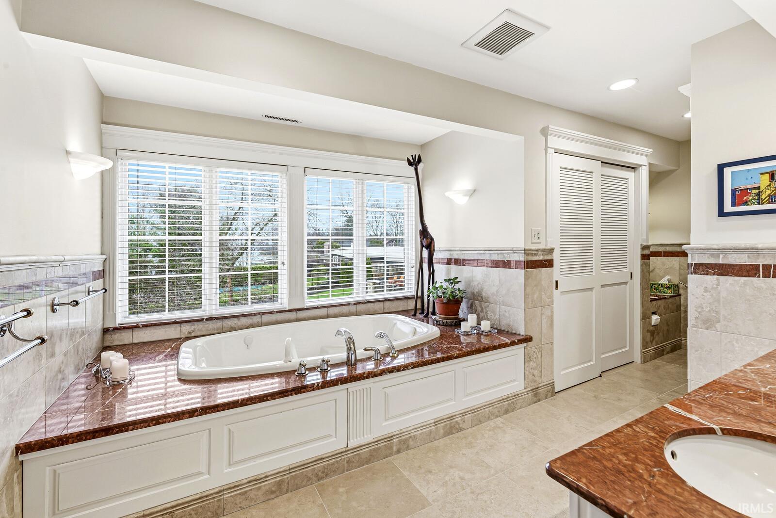 Full bath featuring tile walls, a wainscoted wall, a bath, vanity, and light tile patterned flooring