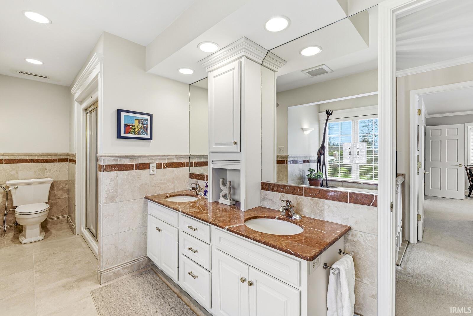 Full bath featuring double vanity, tile walls, wainscoting, and recessed lighting