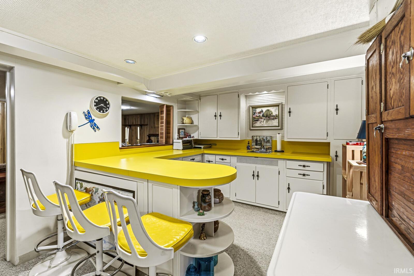 Kitchen featuring open shelves, a peninsula, light countertops, white cabinets, and a breakfast bar