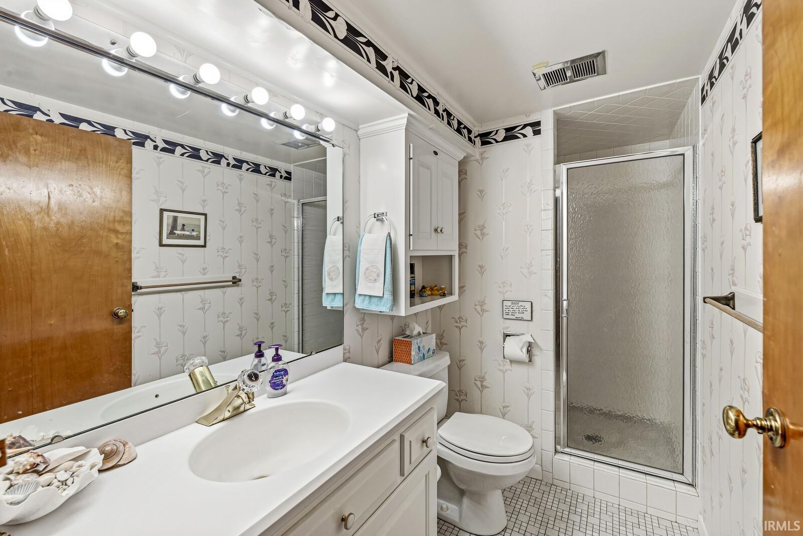 Full bathroom with wallpapered walls, vanity, a shower stall, and light tile patterned floors