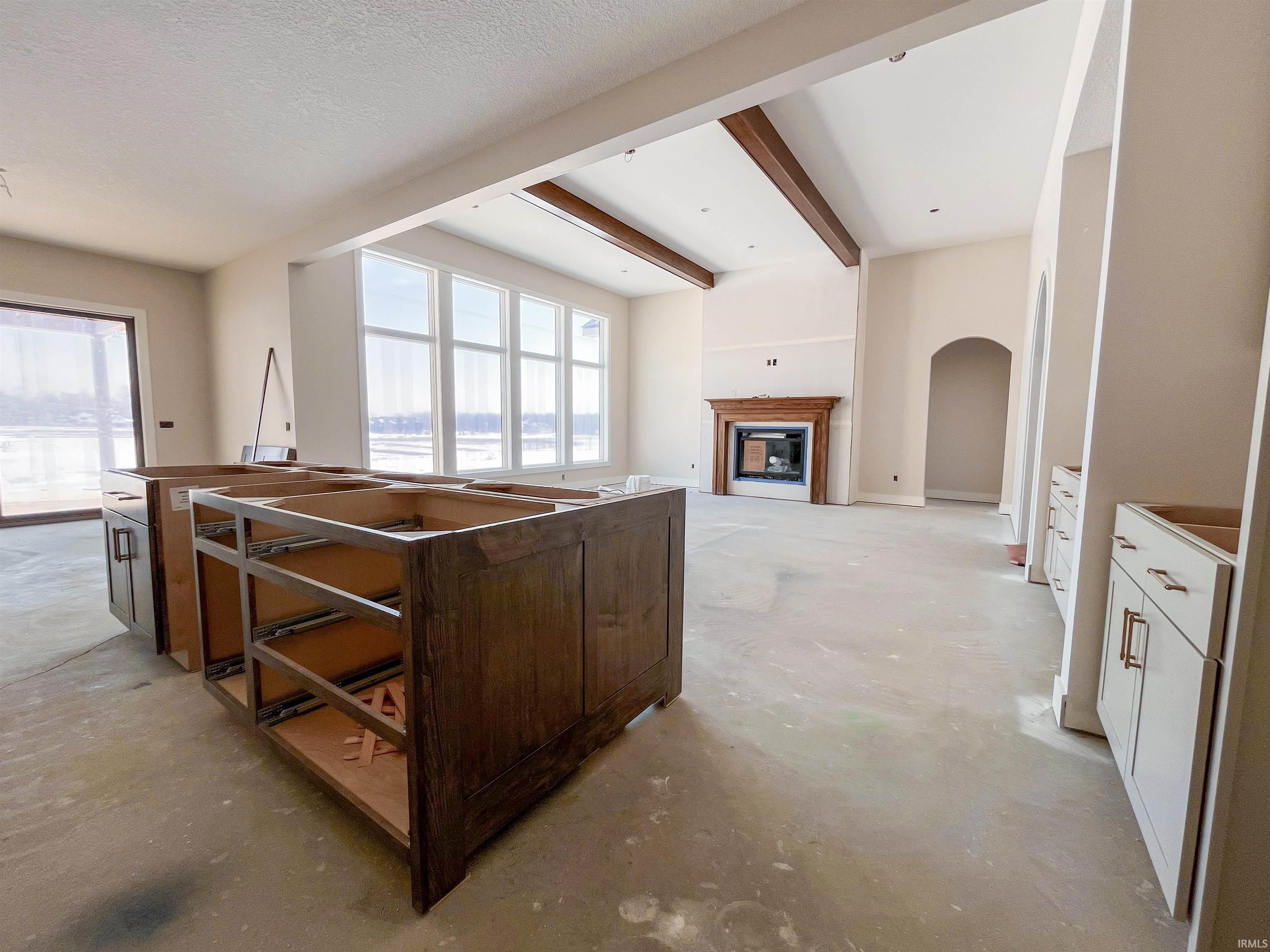 Kitchen featuring a glass covered fireplace, unfinished concrete floors, beam ceiling, and arched walkways