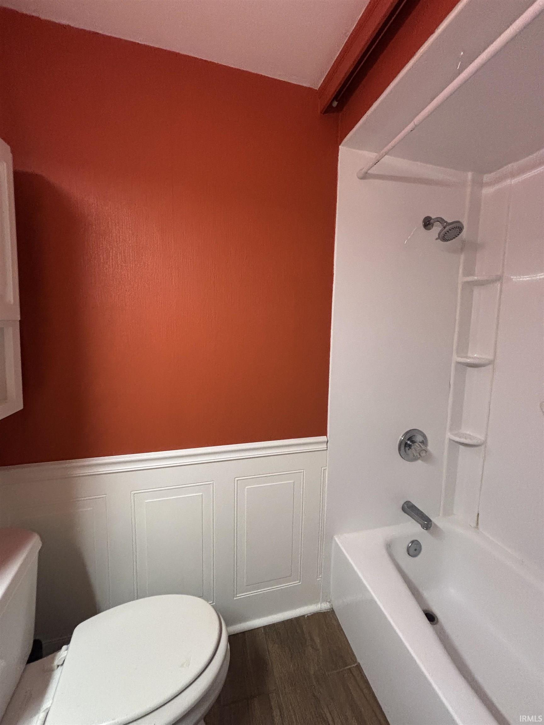 Bathroom featuring  shower combination, dark wood-style flooring, wainscoting, and a decorative wall