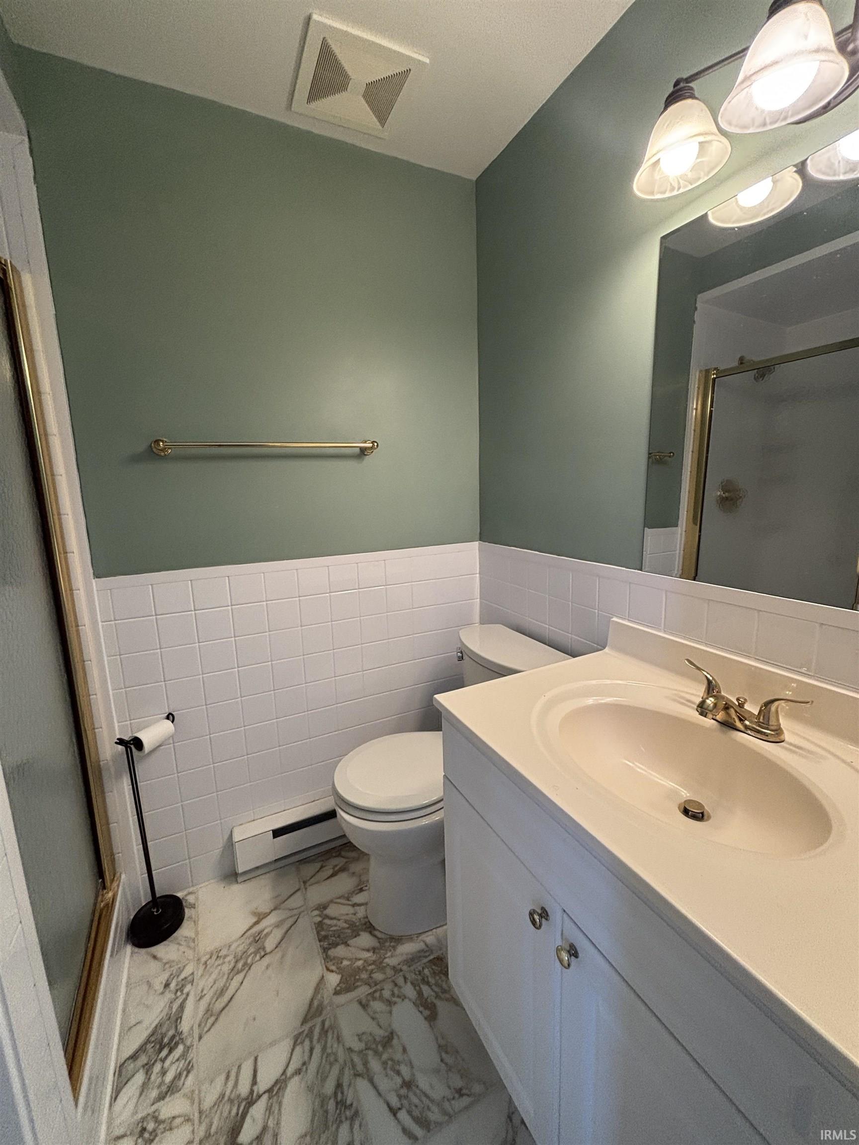 Bathroom with a stall shower, tile walls, vanity, wainscoting, and baseboard heating
