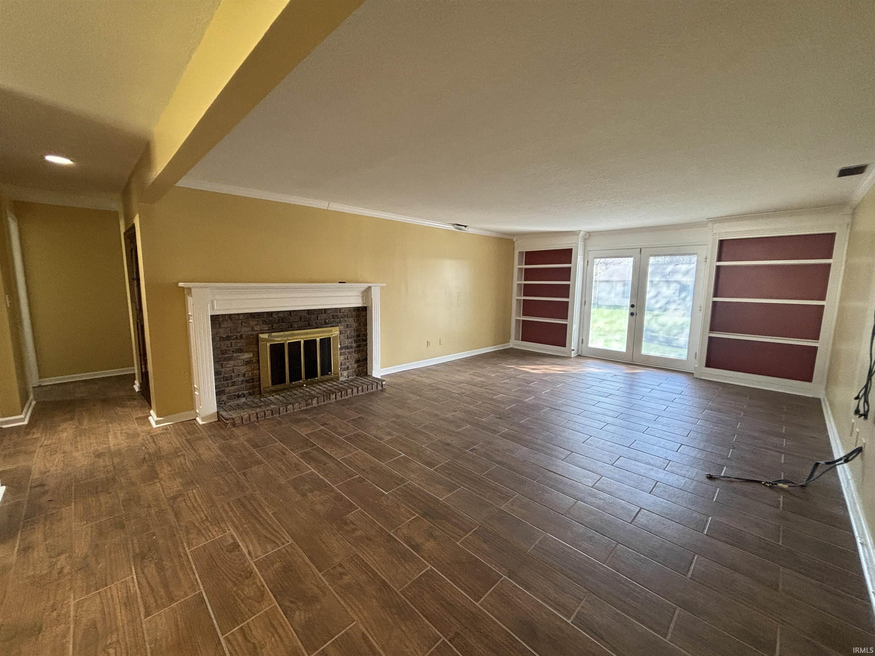 Unfurnished living room featuring built in shelves, crown molding, wood finish floors, a fireplace, and french doors