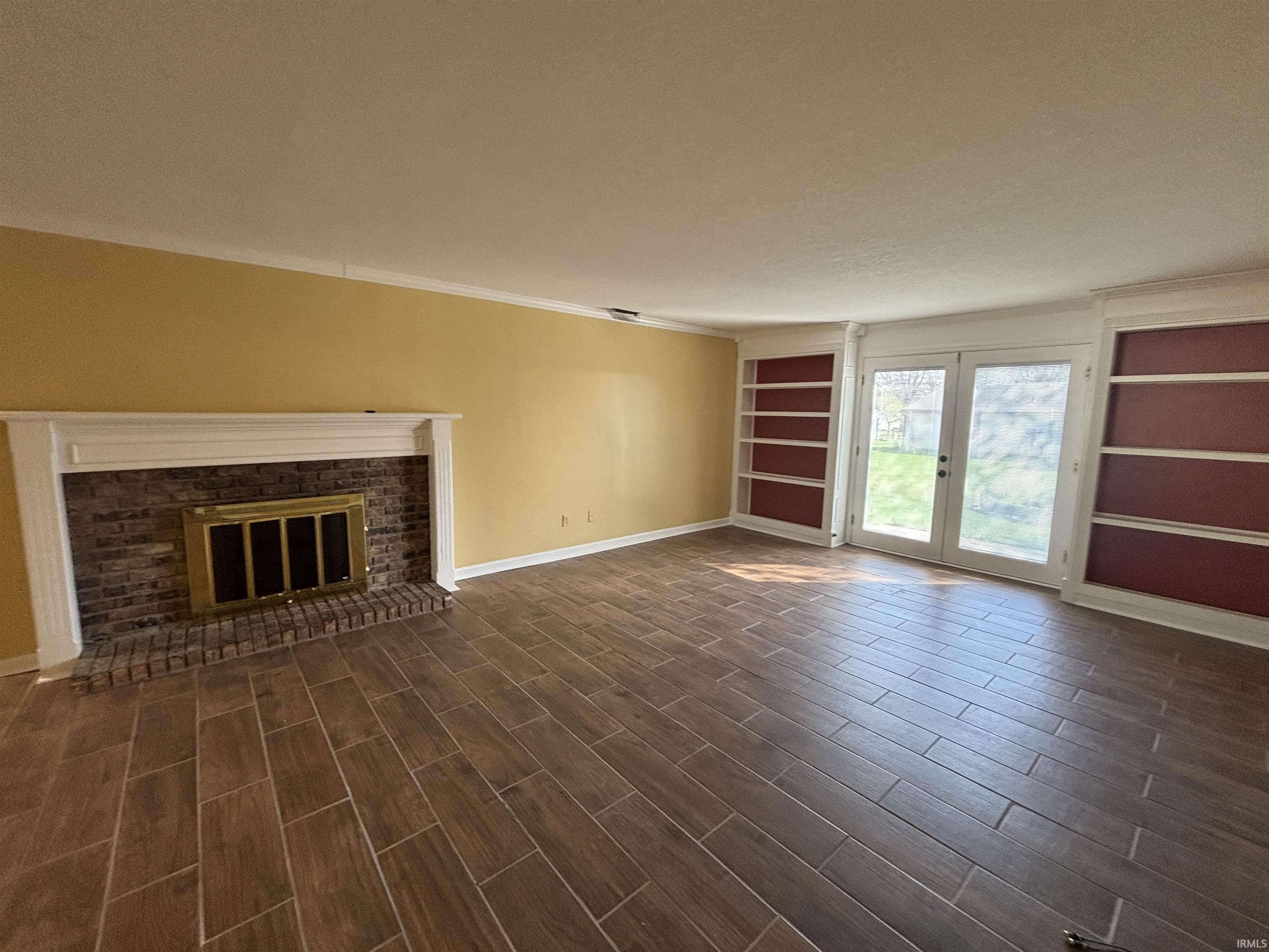 Unfurnished living room featuring built in shelves, wood tiled floors, a brick fireplace, and ornamental molding