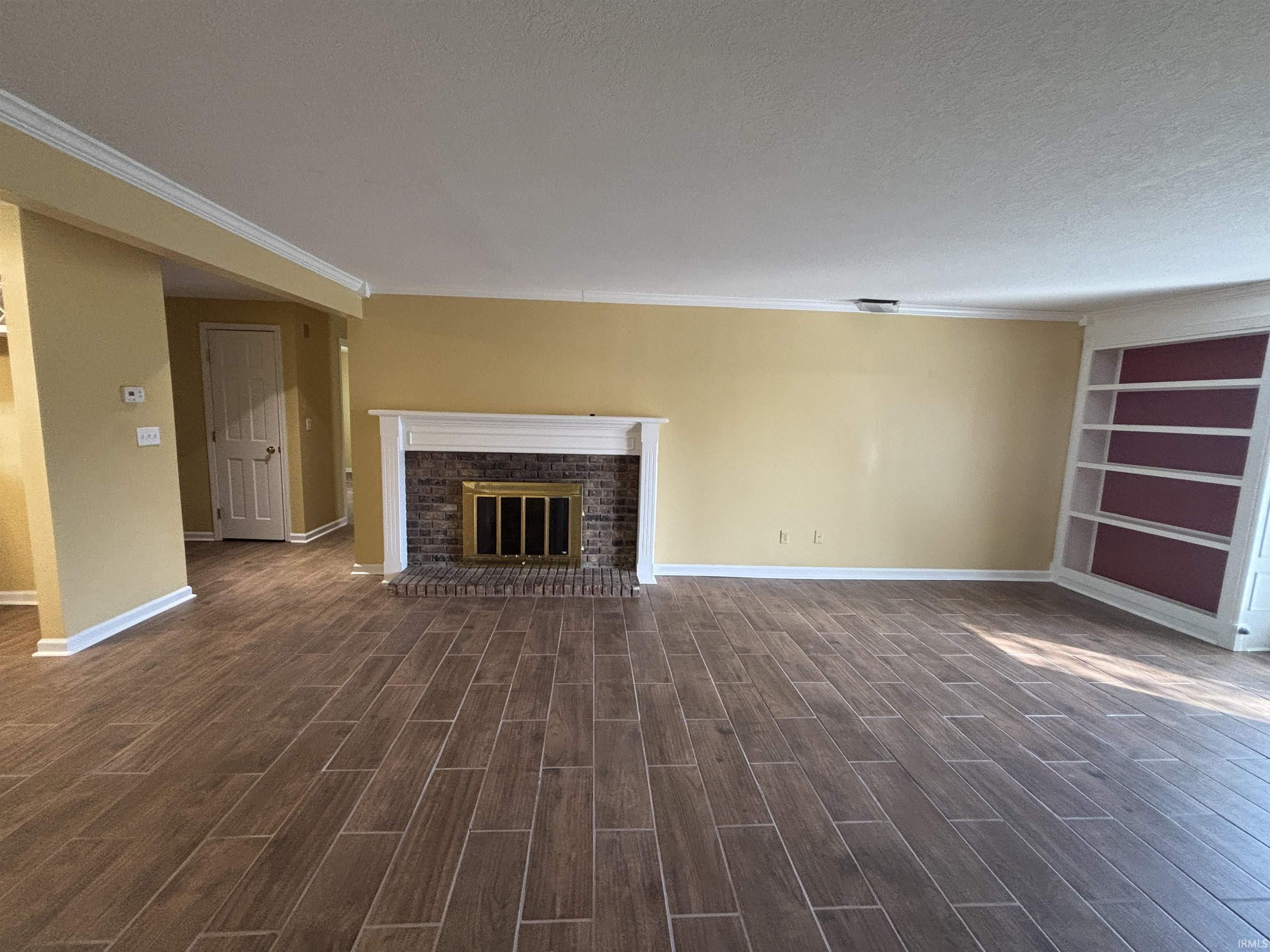Unfurnished living room featuring a brick fireplace, wood finish floors, a textured ceiling, ornamental molding, and built in shelves