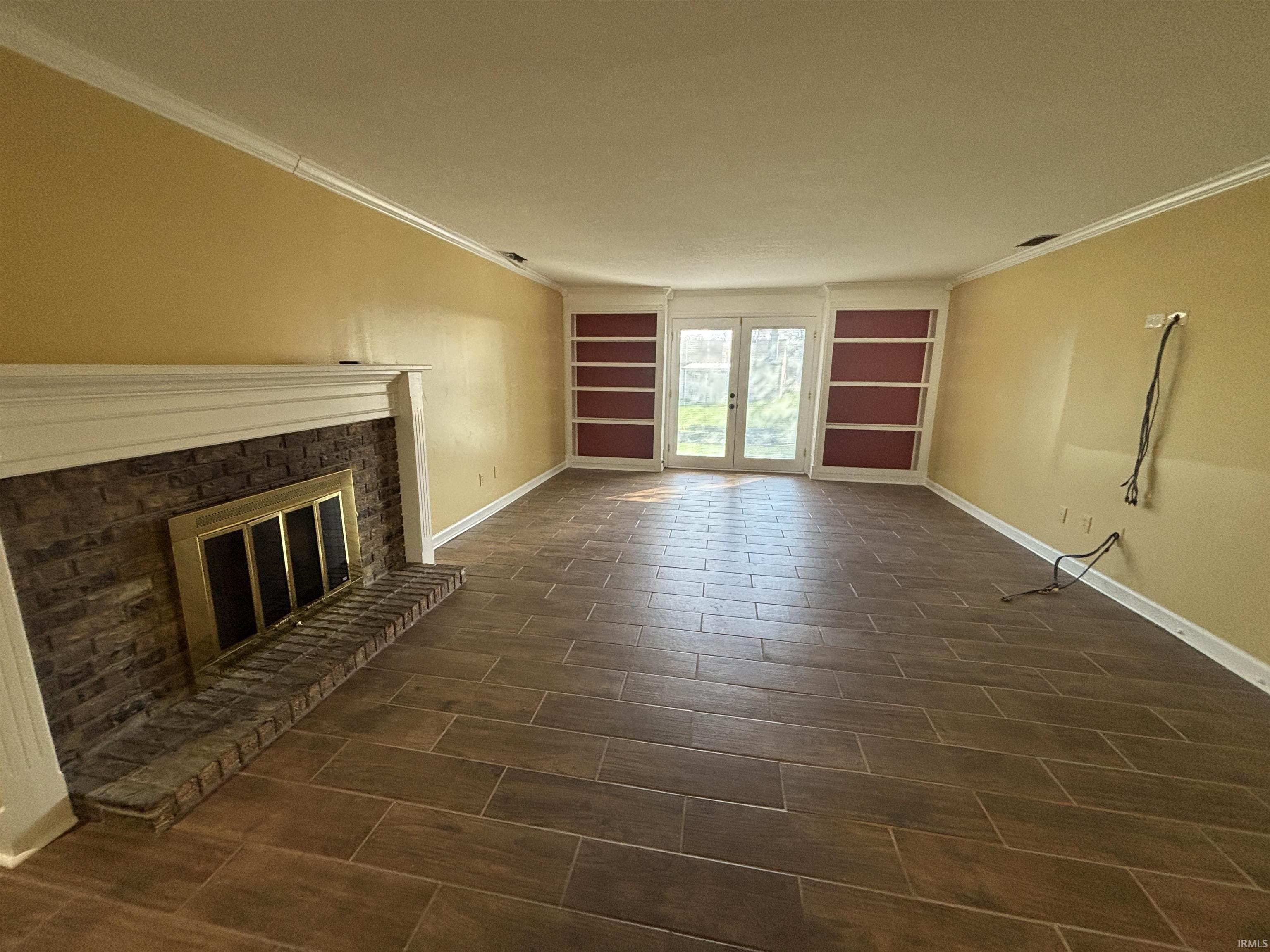 Unfurnished living room with crown molding, wood tiled floors, a fireplace, french doors, and built in shelves