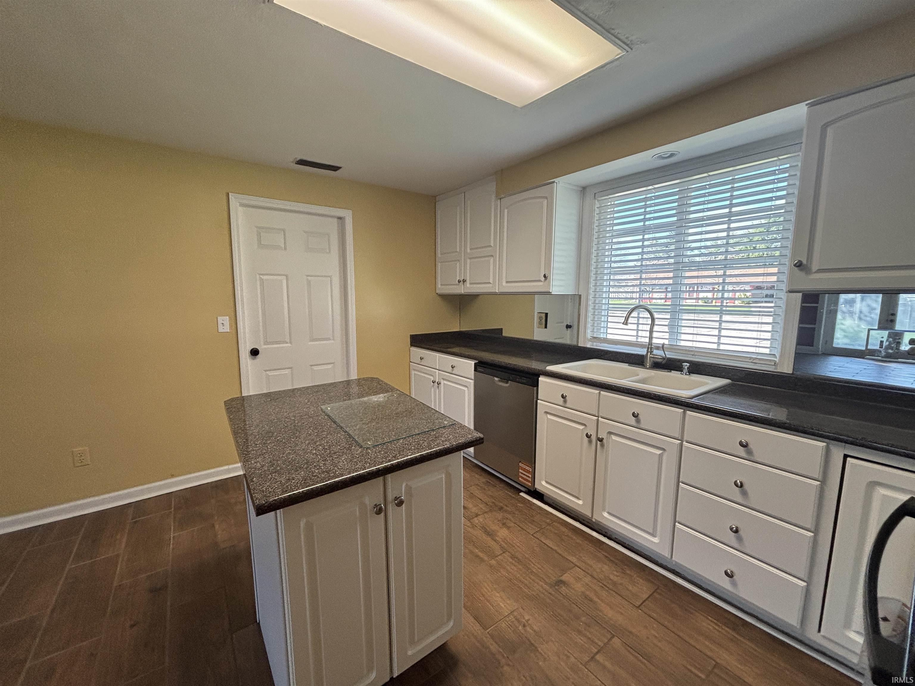 Kitchen with dark countertops, white cabinetry, dark wood-type flooring, dishwasher, and a kitchen island