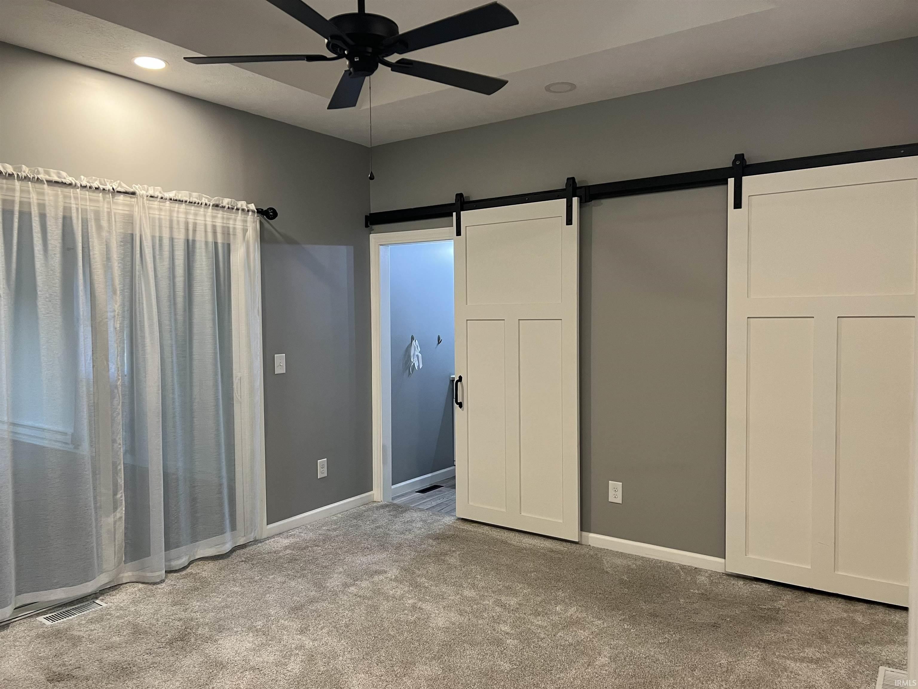 Bedroom featuring gray walls, gray carpeting, a tray ceiling, and a ceiling fan with light fixture