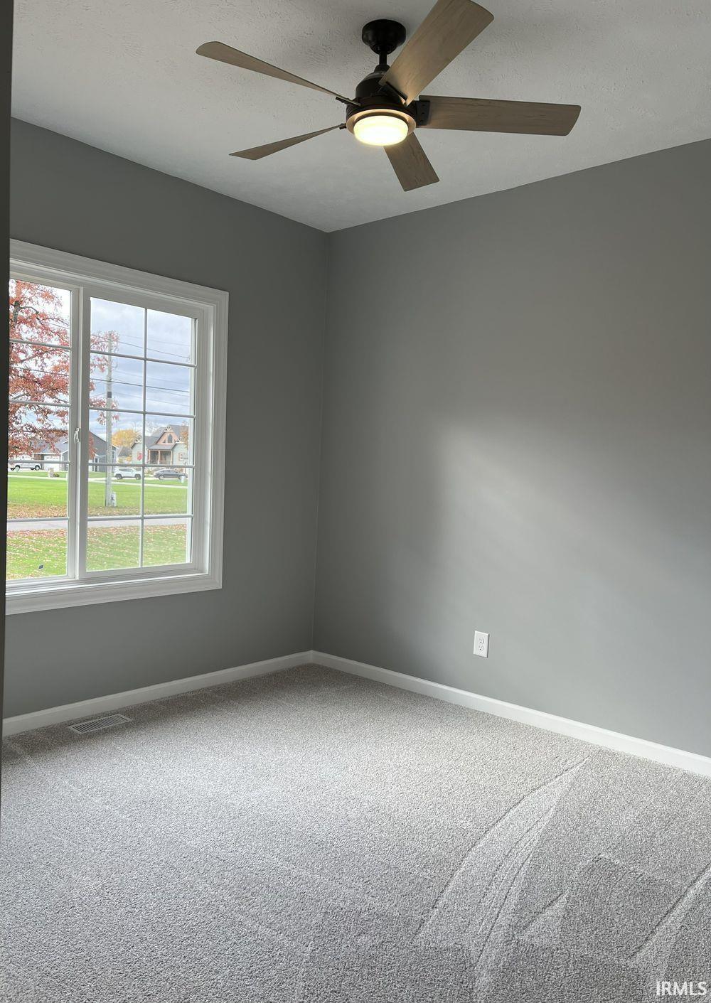 Carpeted spare room featuring ceiling fan and baseboards