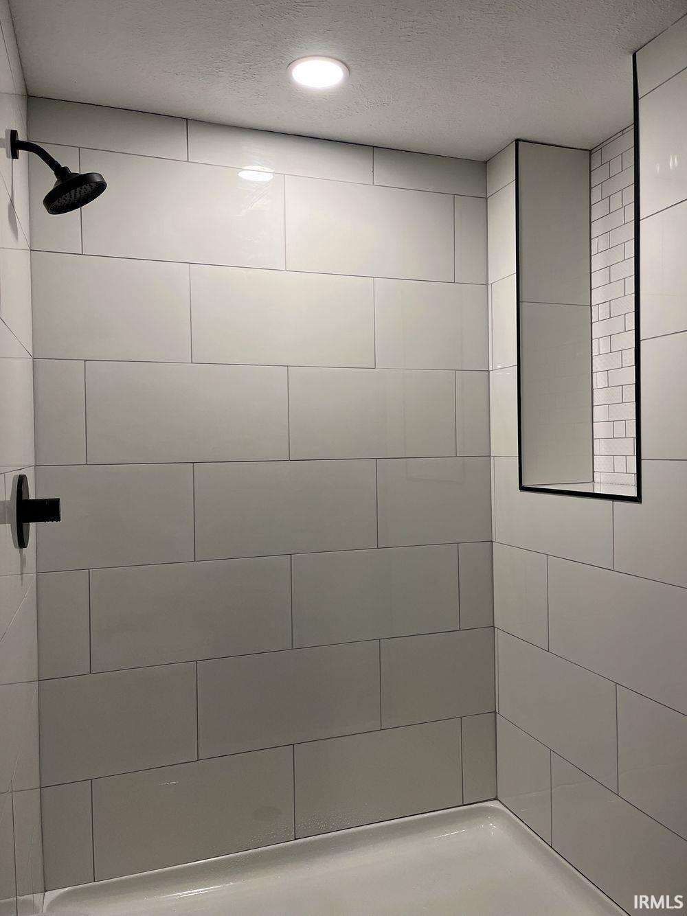 Full bath featuring a textured ceiling, tiled shower, and recessed lighting