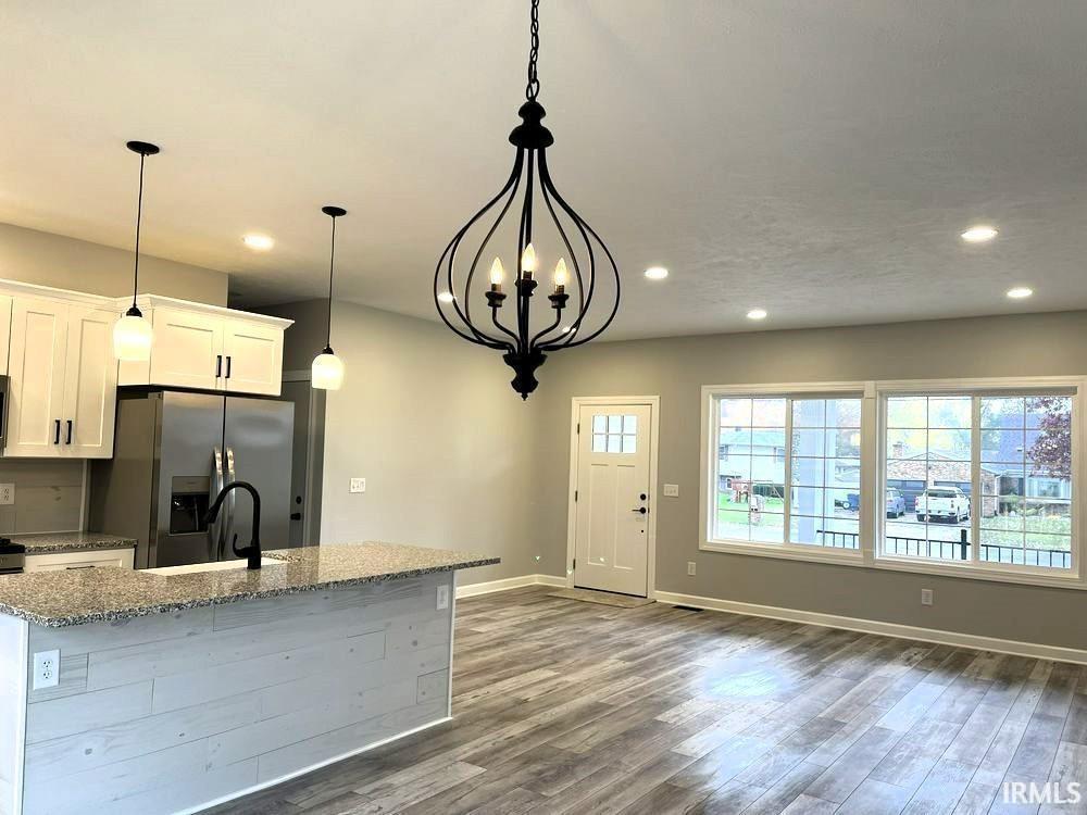 Kitchen with light stone countertops, suspended lighting, white cabinets, and dark wood-style flooring