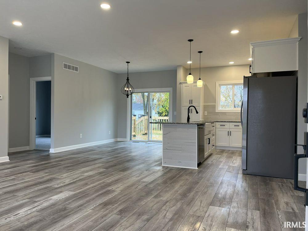 Kitchen with white cabinets, stainless steel appliances, light wood finished floors, and dark stone counters