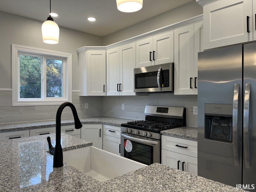 Kitchen featuring stainless steel appliances, white cabinetry, hanging light fixtures, and light stone counters