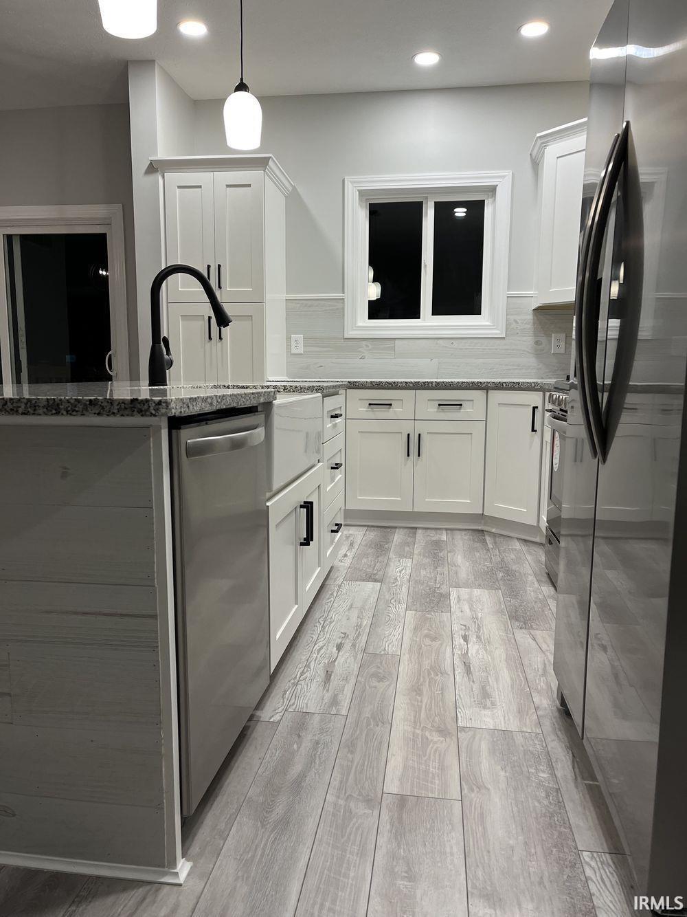 Kitchen featuring white cabinetry, light stone countertops, stainless steel appliances, tasteful backsplash, and light wood-type flooring