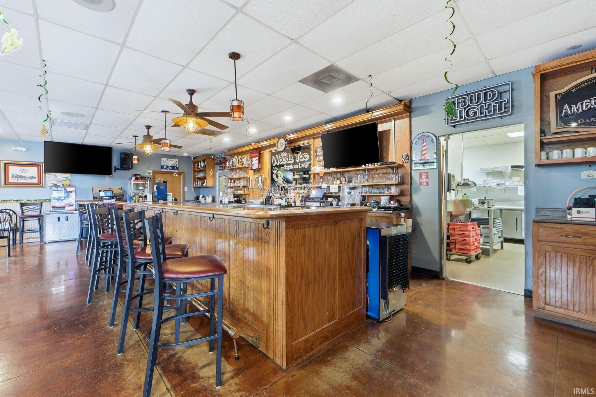 Community bar area with a paneled ceiling, wood finish cabinetry, hanging light fixtures, ceiling fan, and open shelves