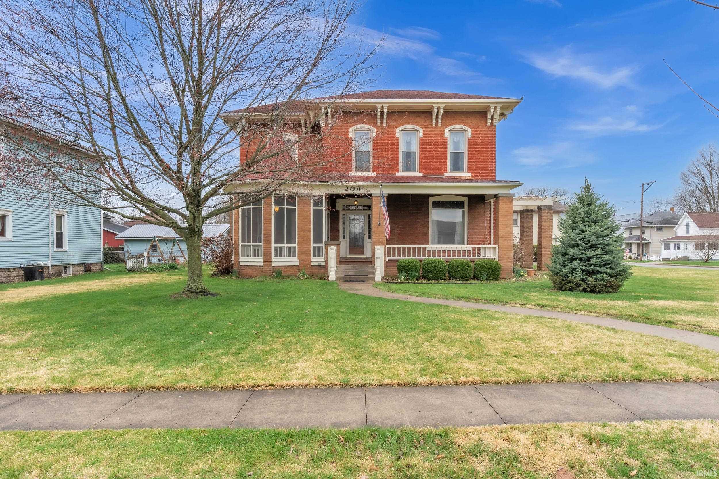Italianate-style house with brick siding, covered porch, and a front lawn
