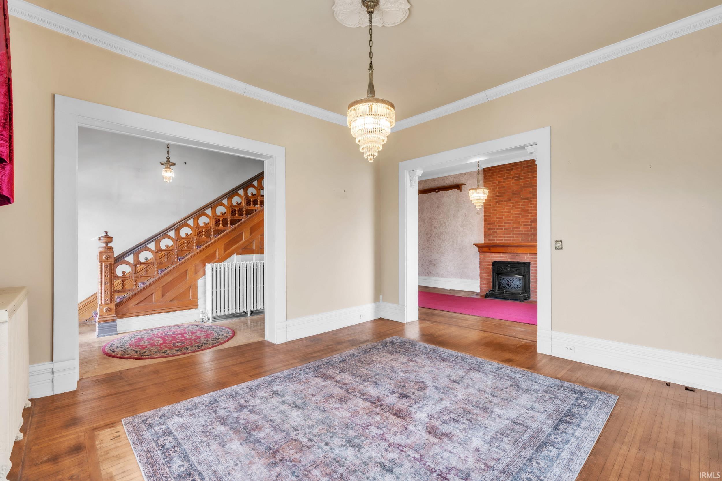 Dining room featuring ornamental molding, radiator heating unit, wood-type flooring, a brick fireplace, and hanging lights