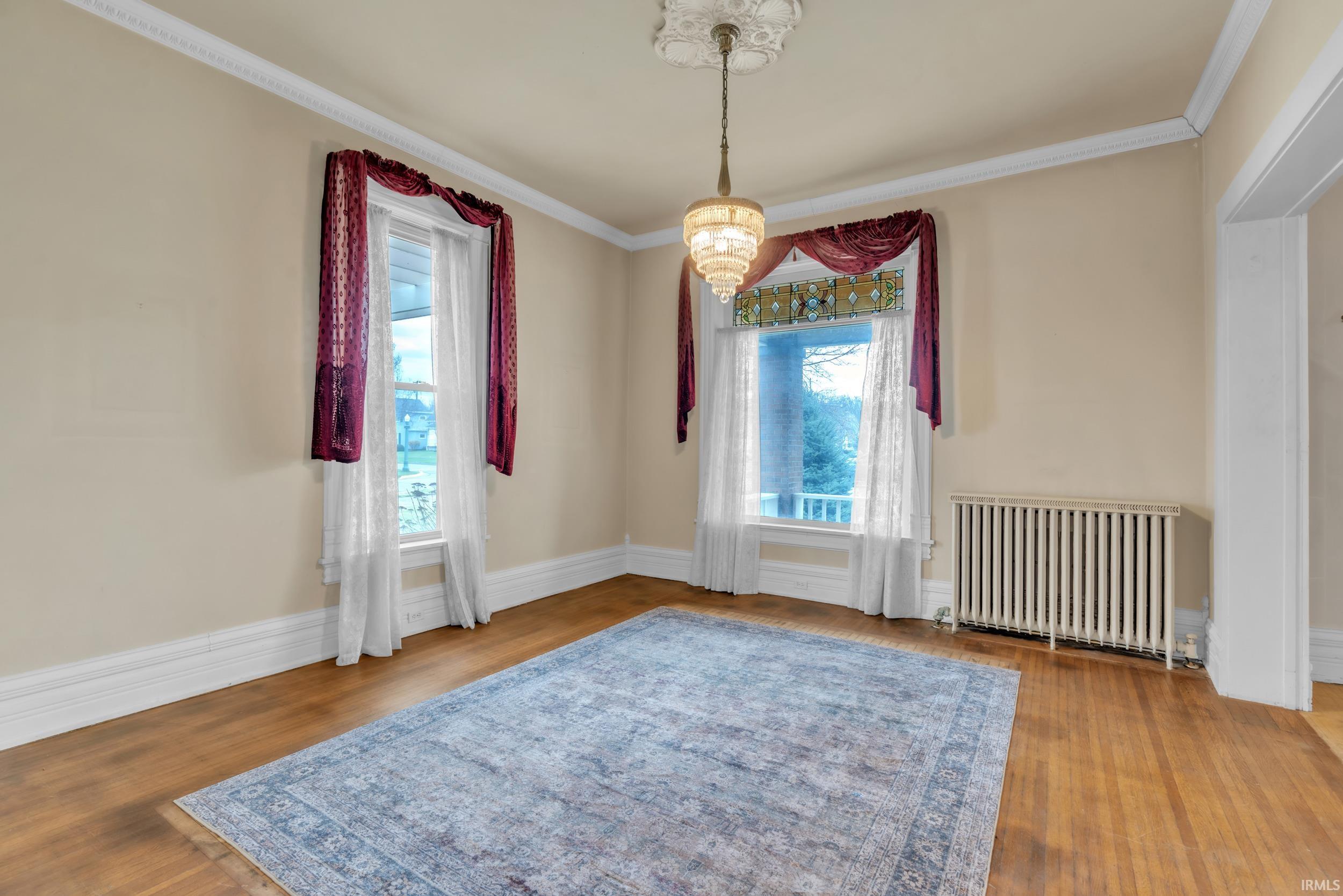 Unfurnished room with radiator, crown molding, wood finished floors, and hanging lights