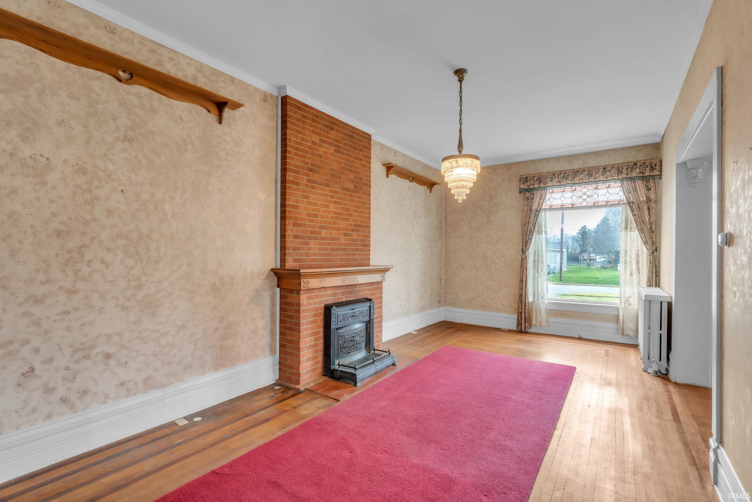 Unfurnished living room featuring hardwood / wood-style flooring, a fireplace, ornamental molding, and wallpapered walls