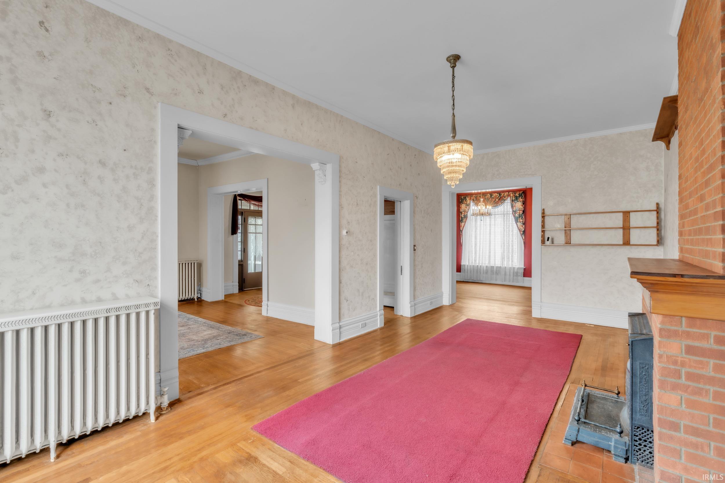 Unfurnished dining area with radiator heating unit, light wood finished floors, ornamental molding, healthy amount of natural light, and wallpapered walls