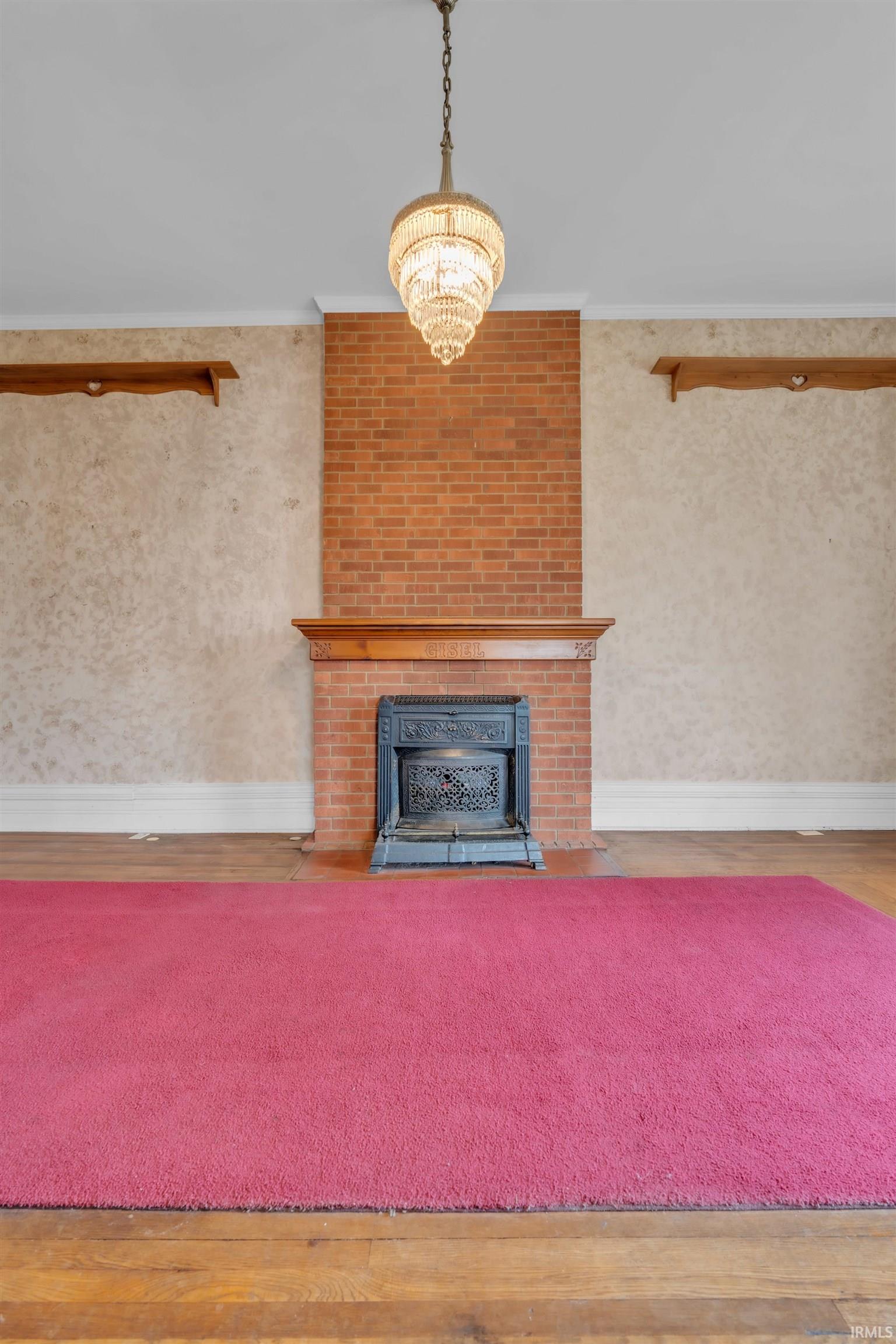 Living room with a fireplace, a chandelier, crown molding, wood finished floors, and wallpapered walls