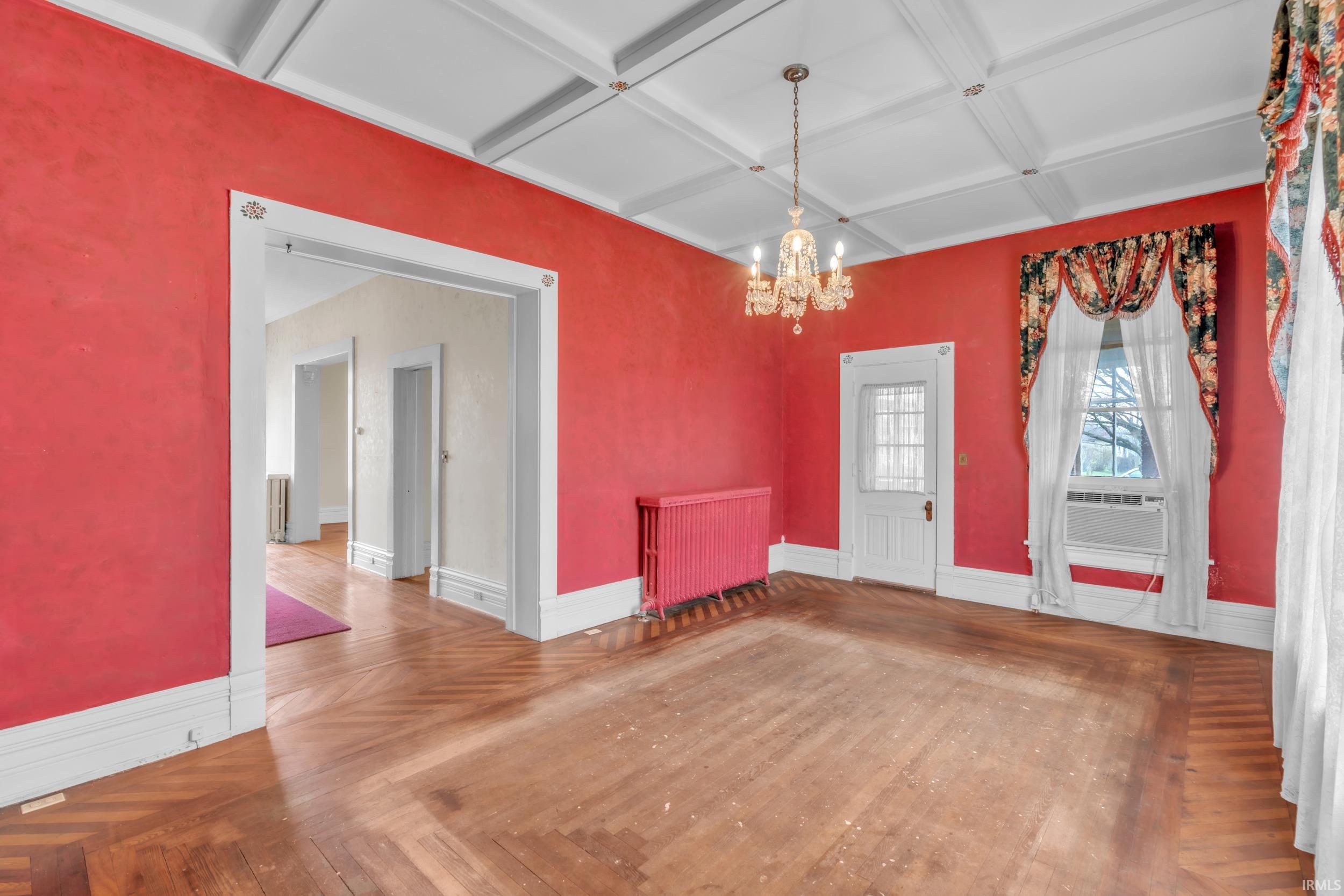 Unfurnished dining area featuring wood finished floors, coffered ceiling, suspended lighting, radiator, and cooling unit
