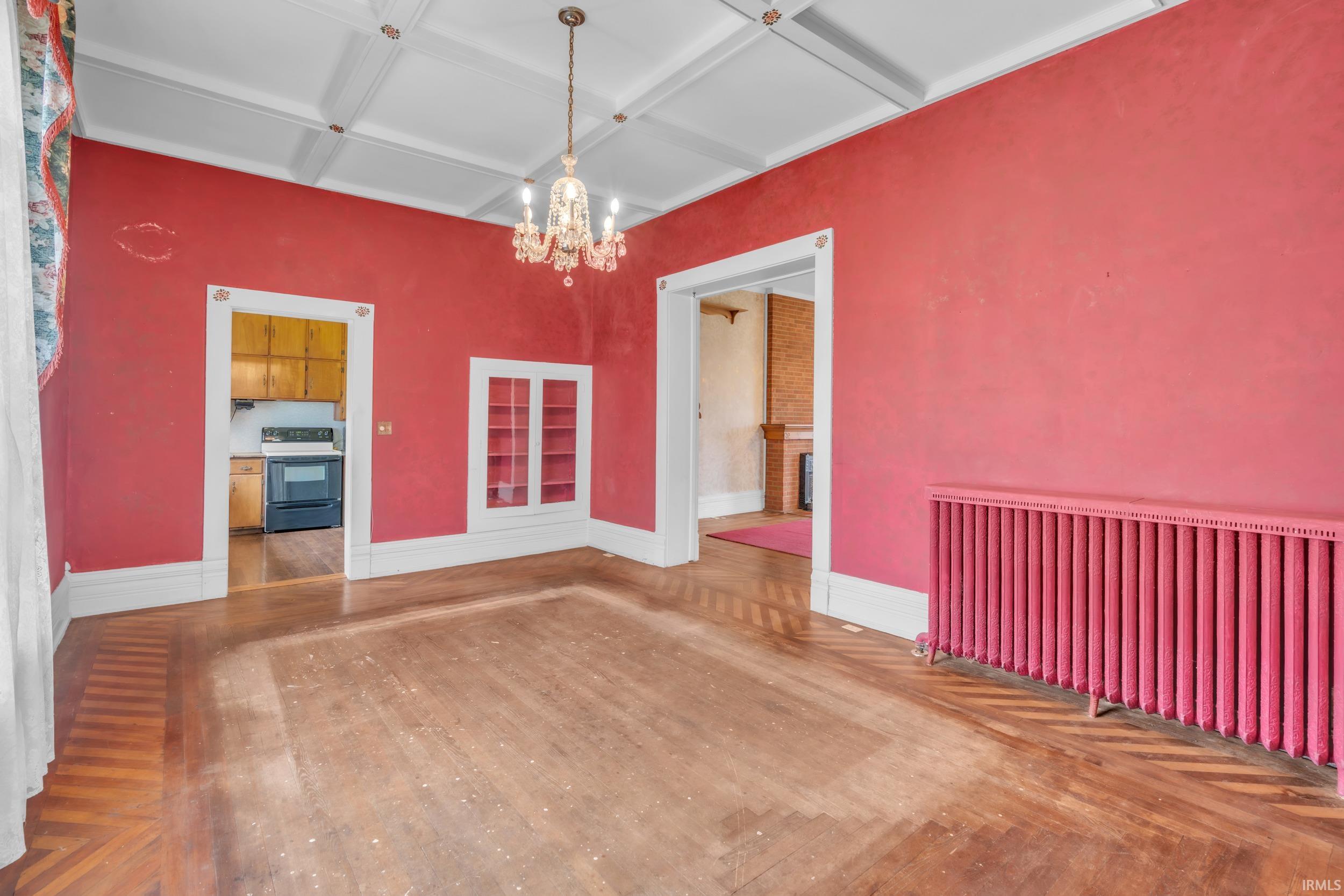 Unfurnished dining area featuring coffered ceiling, hanging lights, wood finished floors, and radiator heating unit