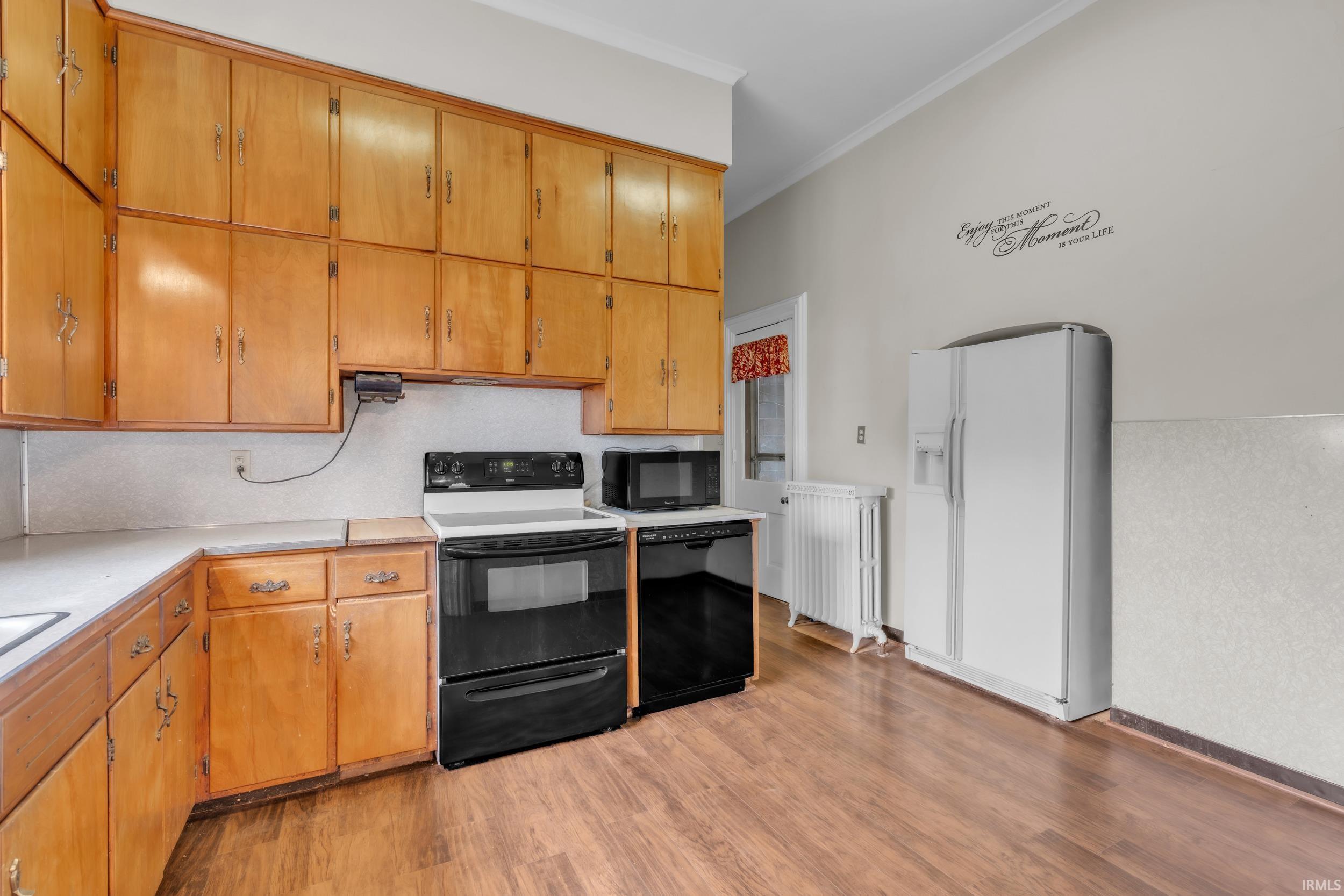Kitchen with black appliances, light countertops, crown molding, light wood-style flooring, and radiator