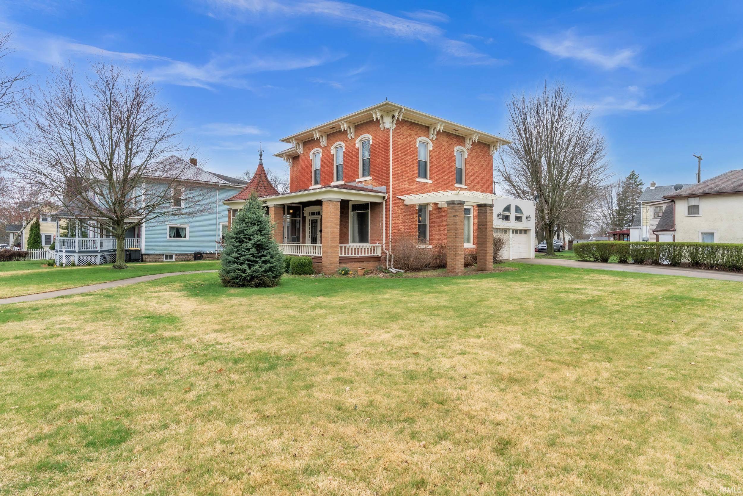 Italianate house with covered porch, brick siding, a front lawn, and driveway
