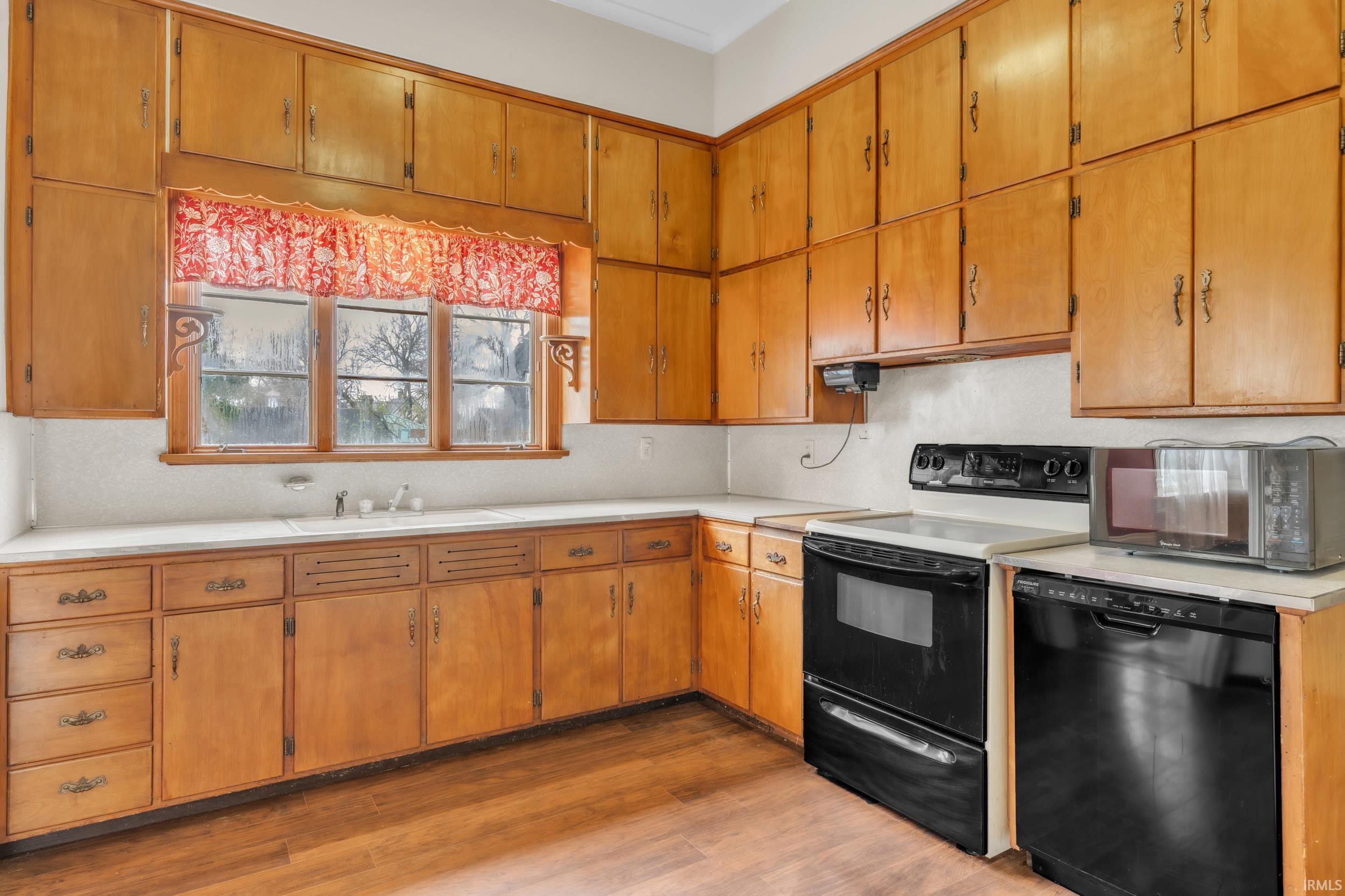 Kitchen featuring light countertops, black appliances, light wood-style floors, and wood finish cabinetry