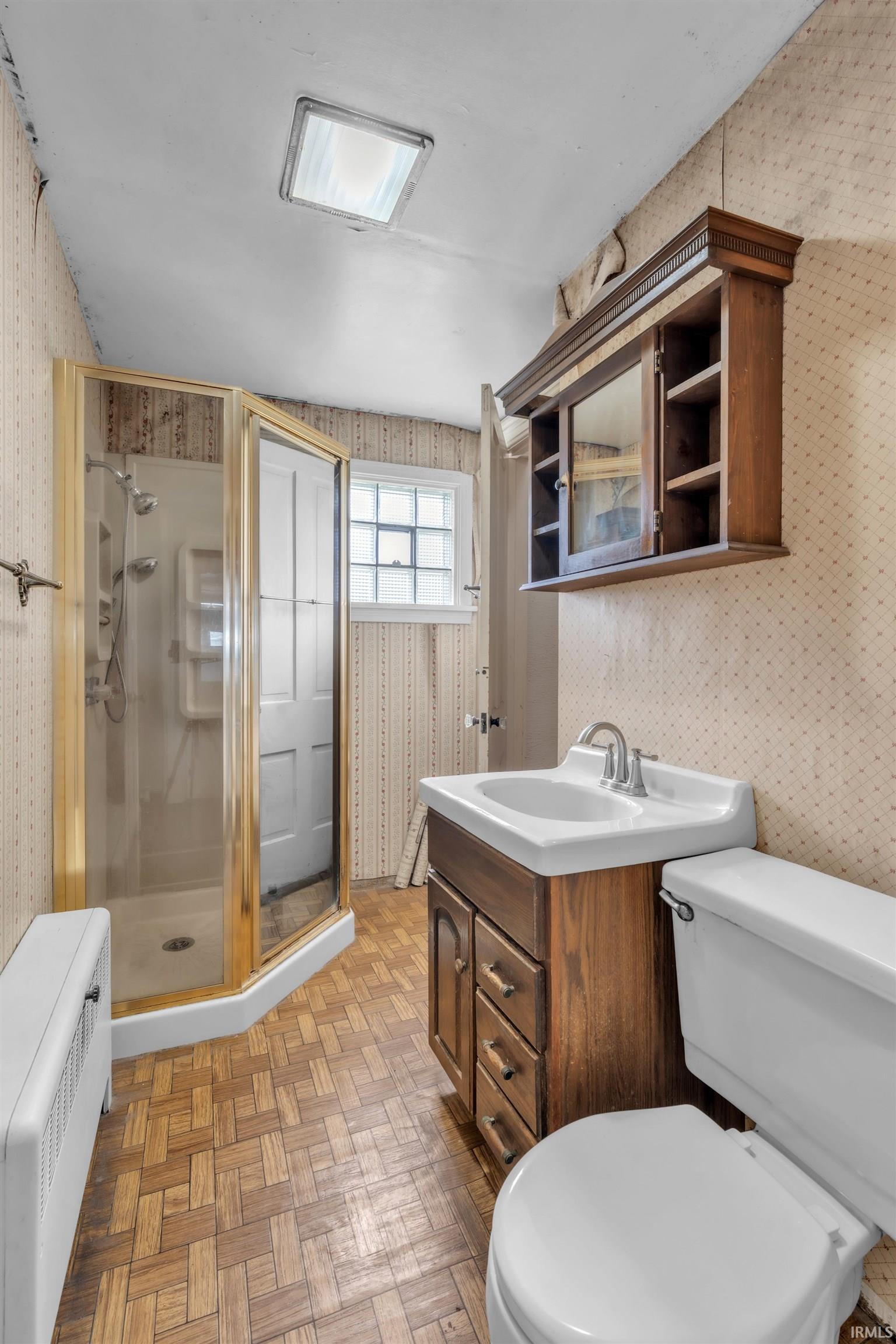 Bathroom with wallpapered walls, vanity, a stall shower, parquet flooring, and radiator heating unit