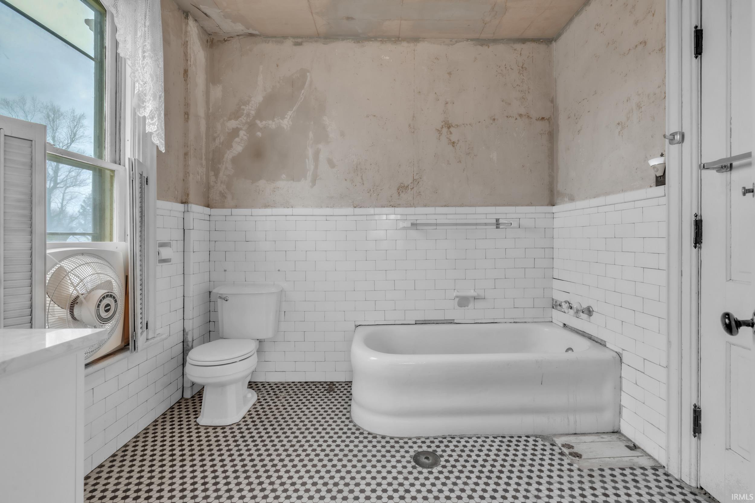 Bathroom featuring a bath, wainscoting, and tile walls