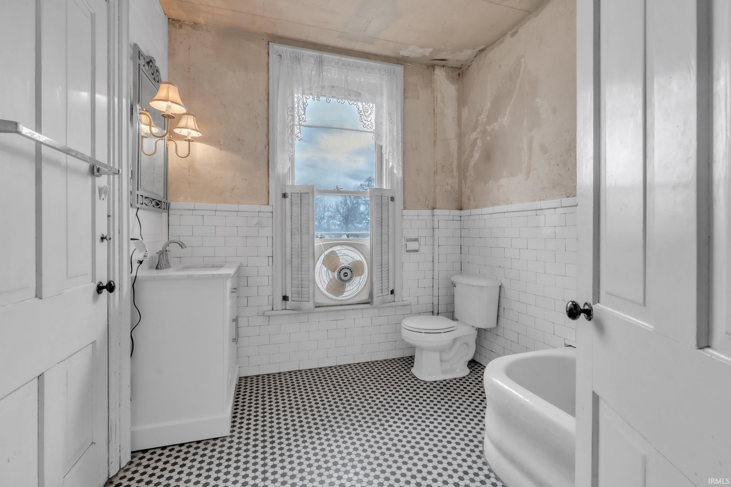 Full bath featuring vanity, wainscoting, and tile walls