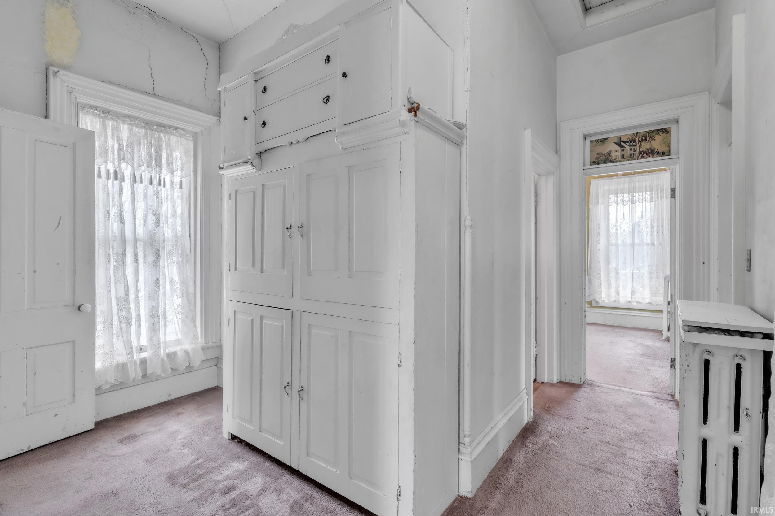 Hallway featuring light colored carpet and radiator heating unit