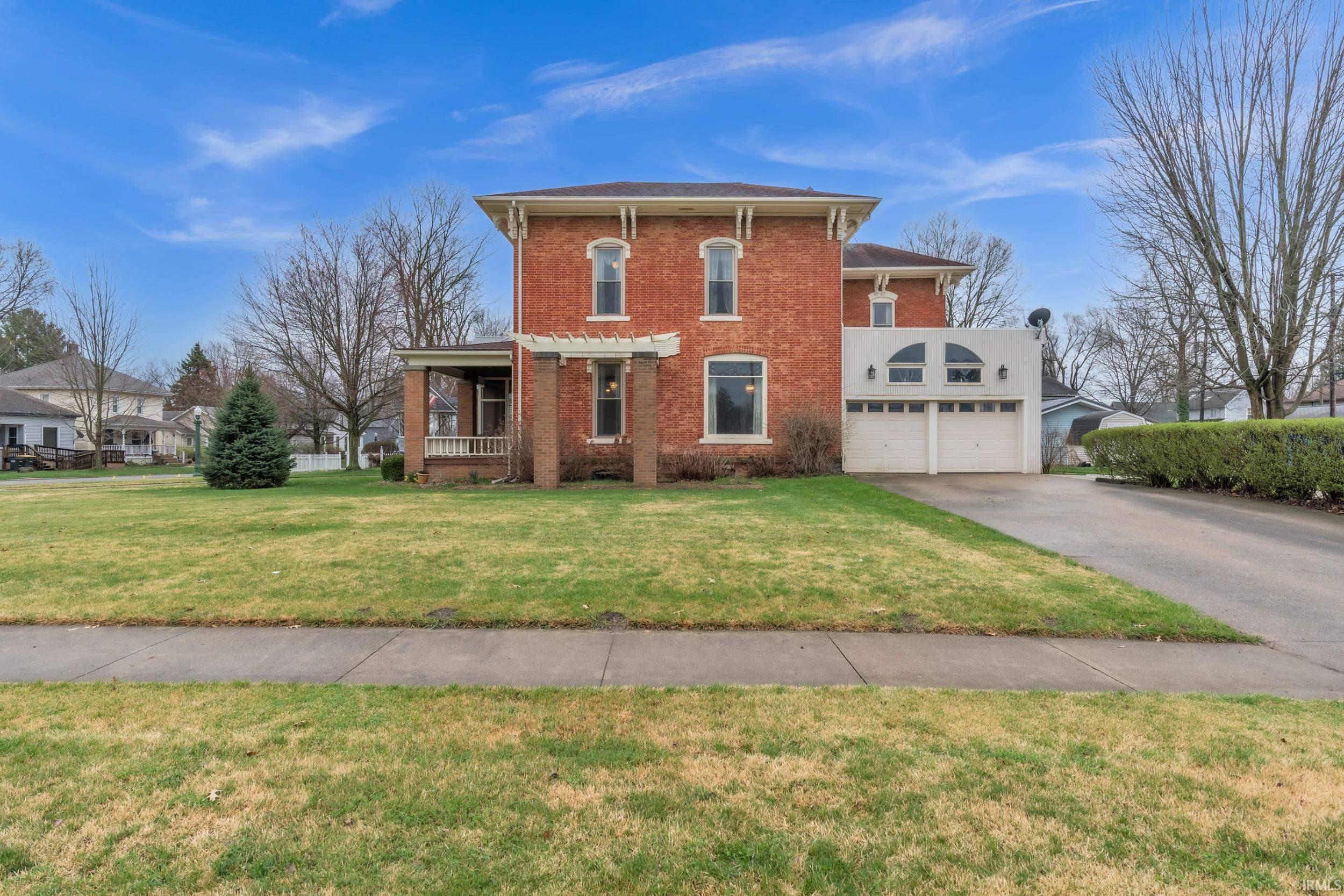 Italianate house featuring brick siding, a front lawn, driveway, and a porch