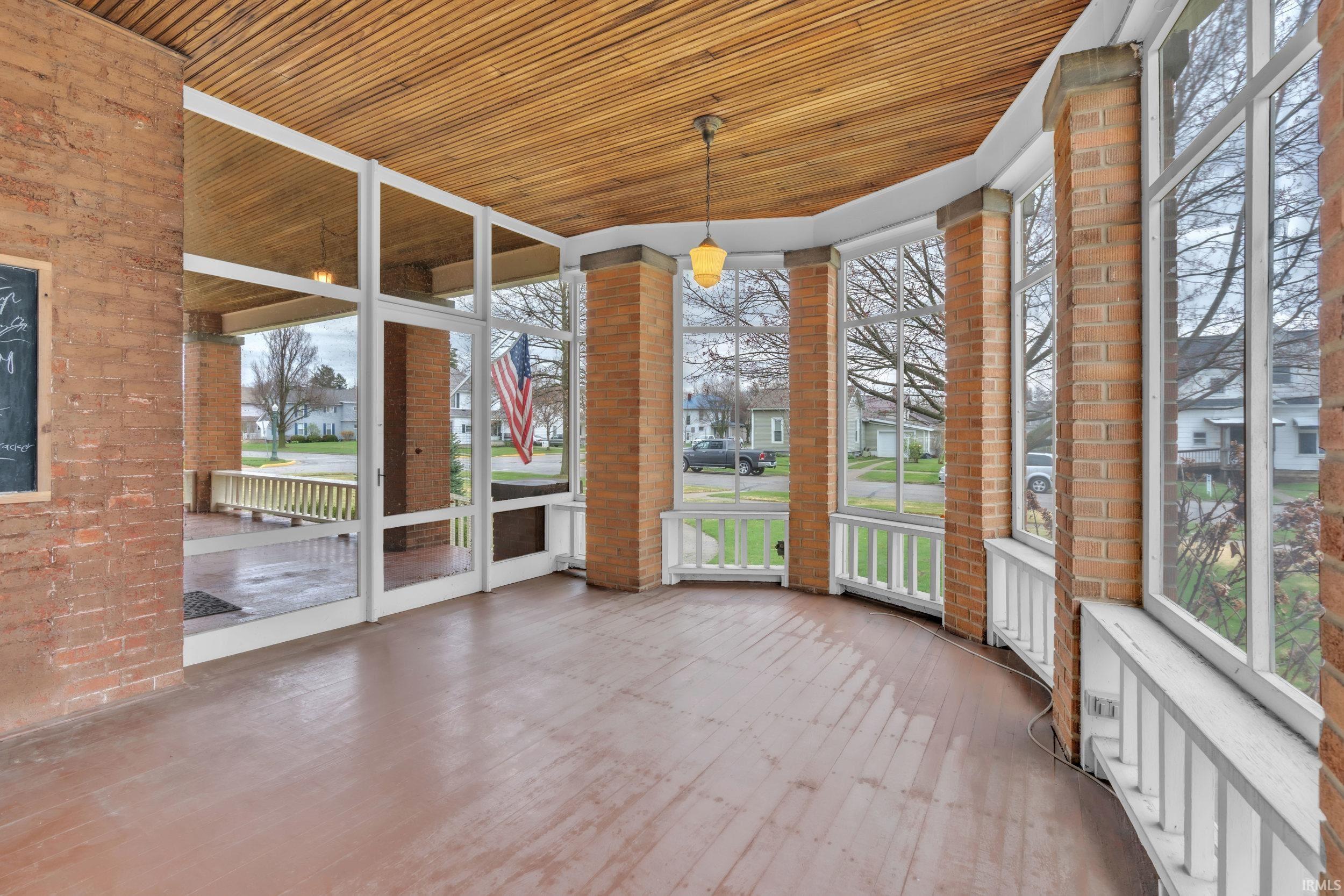 Unfurnished sunroom featuring wooden ceiling, brick wall, a residential view, and wood finished floors