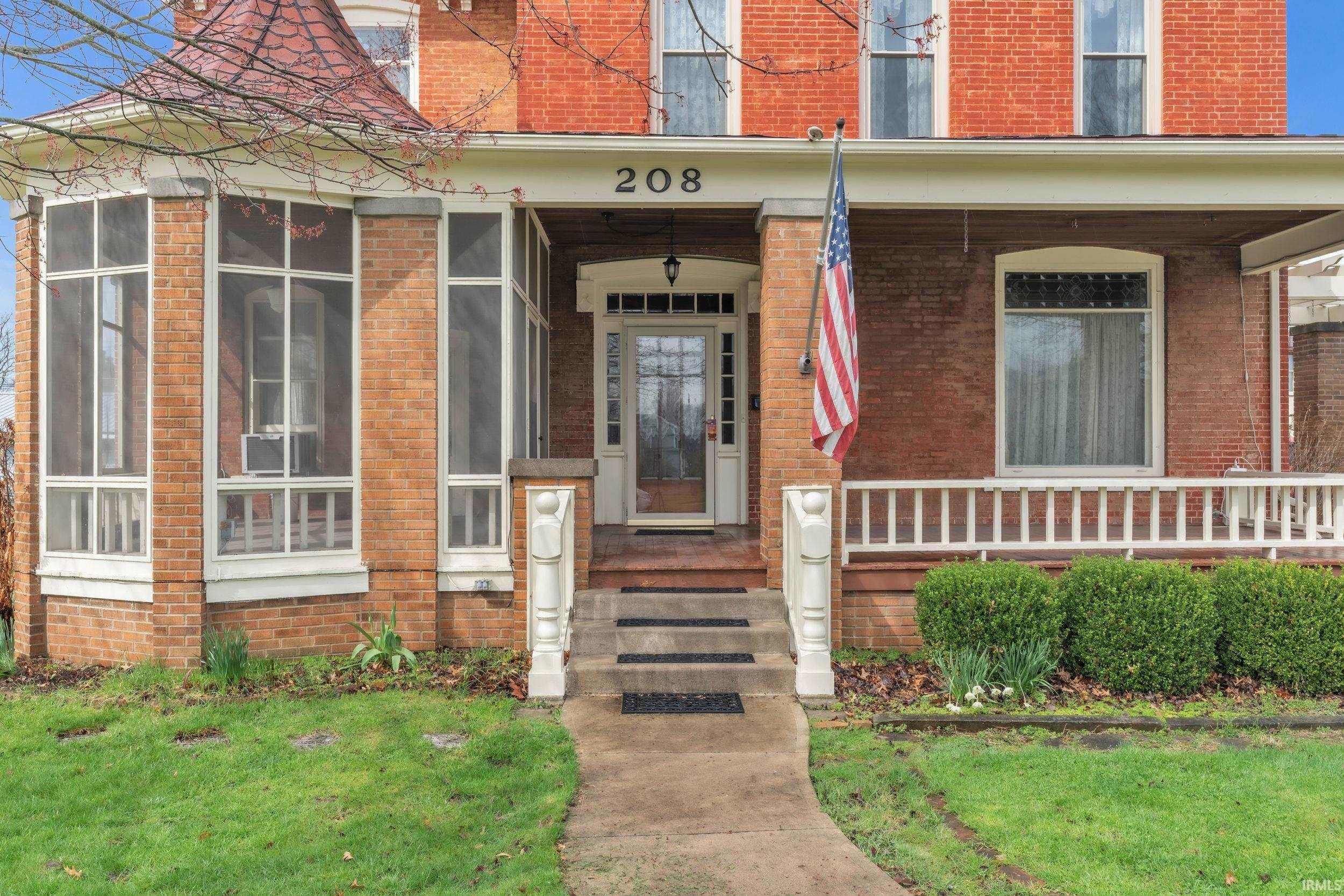 Property entrance with brick siding, covered porch, and a lawn