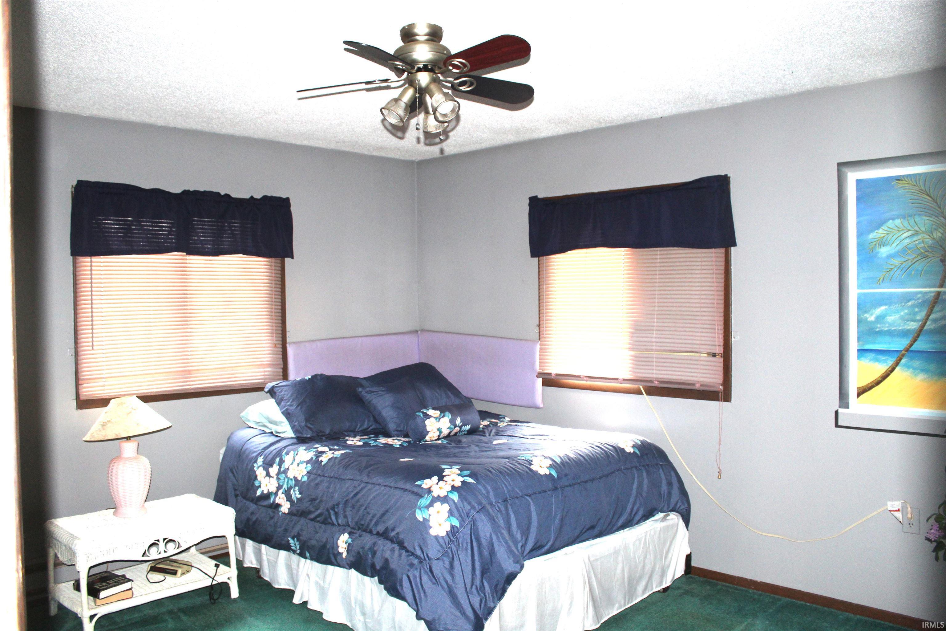 Carpeted bedroom featuring ceiling fan and a textured ceiling