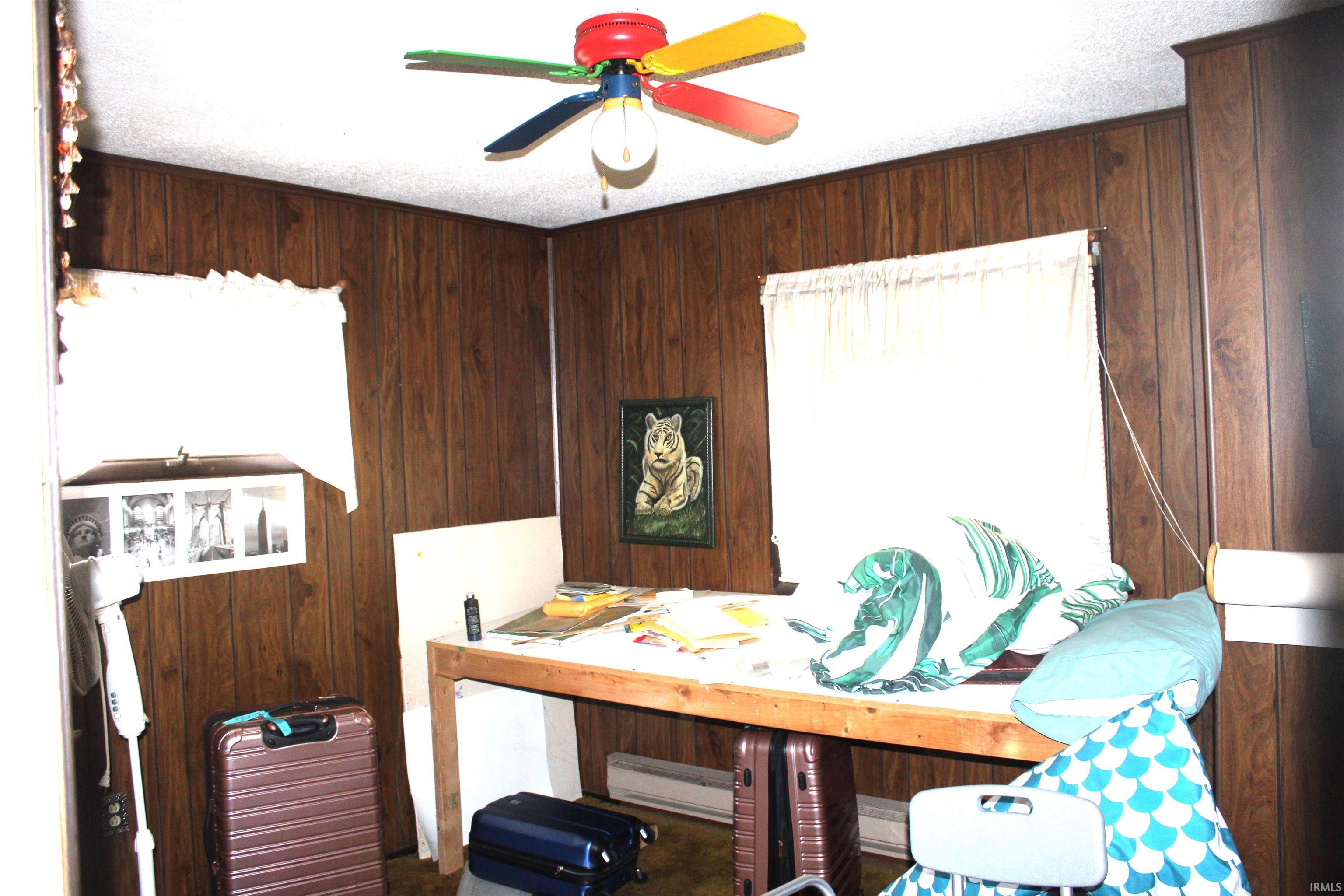 Bedroom with wooden walls, a ceiling fan, and a textured ceiling
