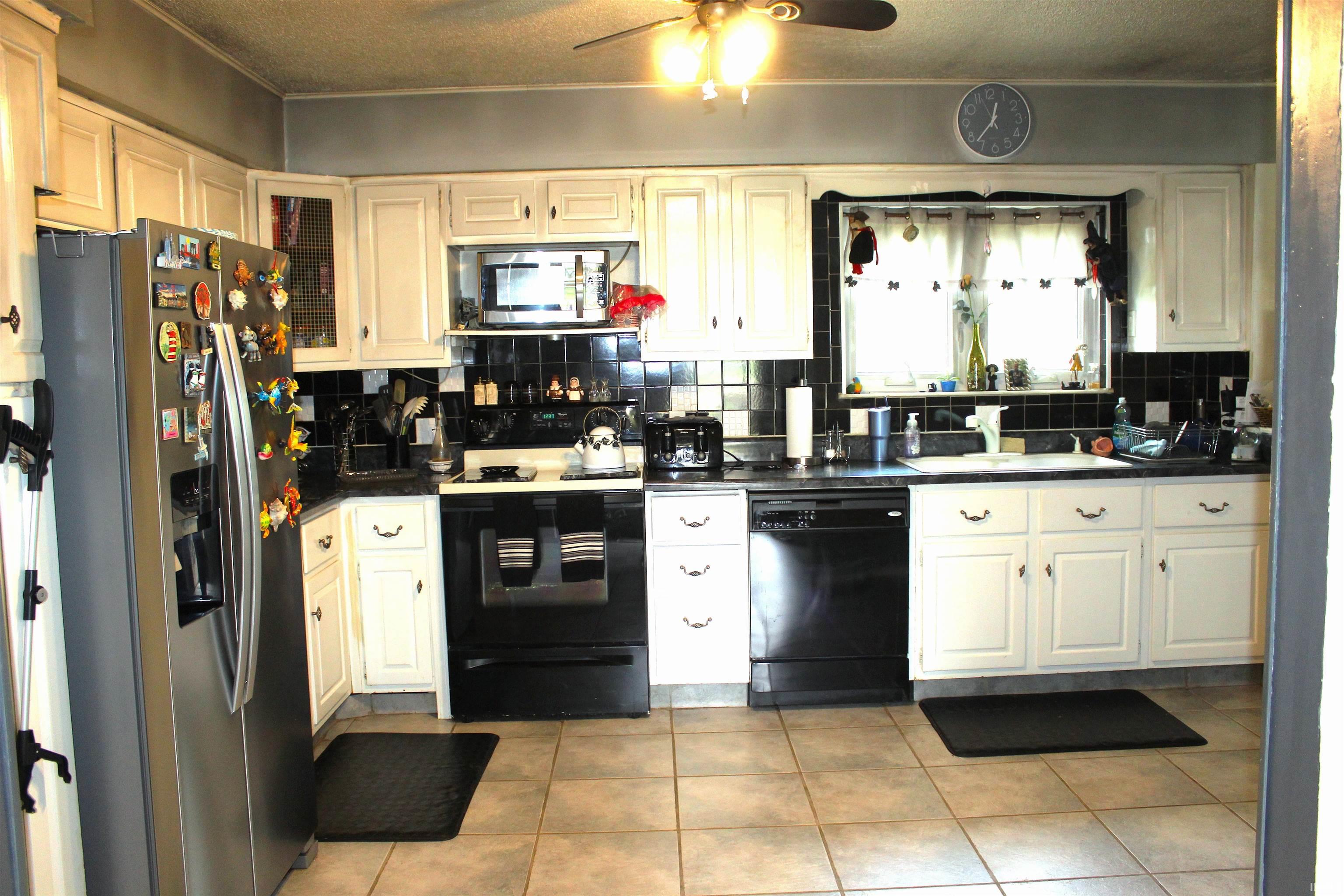 Kitchen featuring black appliances, backsplash, ceiling fan, ornamental molding, and dark countertops