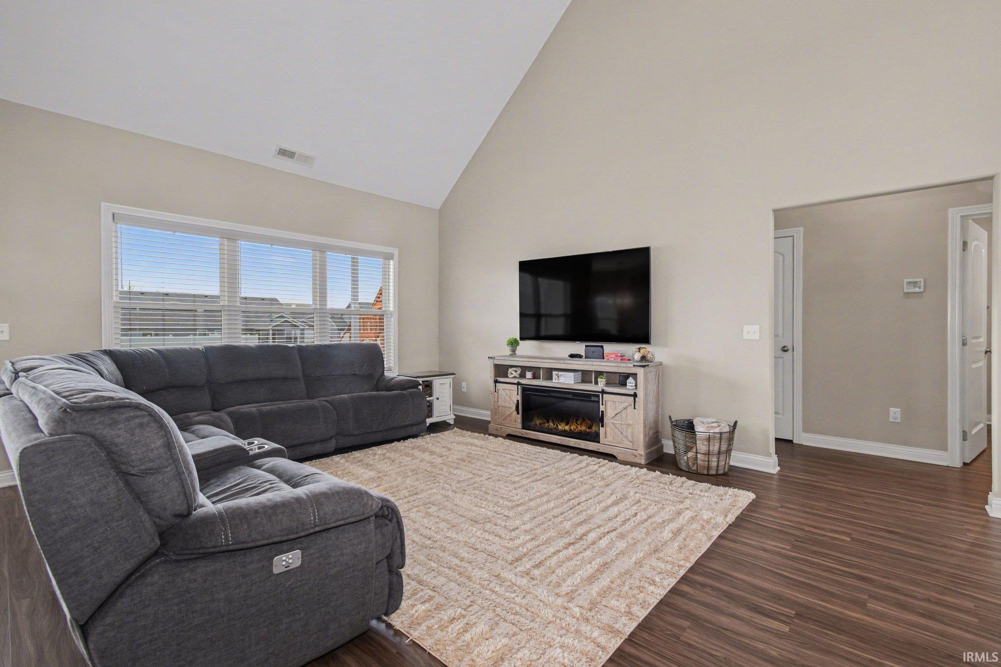 Living area featuring lofted ceiling, dark wood-style flooring, and a warm lit fireplace