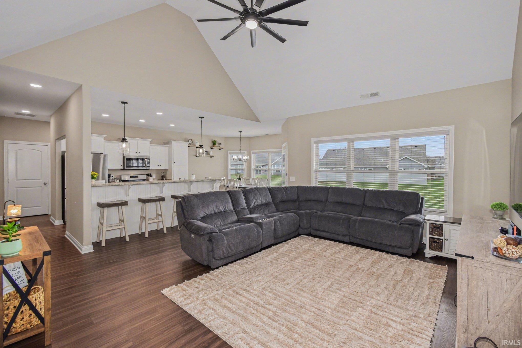 Living room featuring a high ceiling, a ceiling fan, a chandelier, and dark wood finished floors