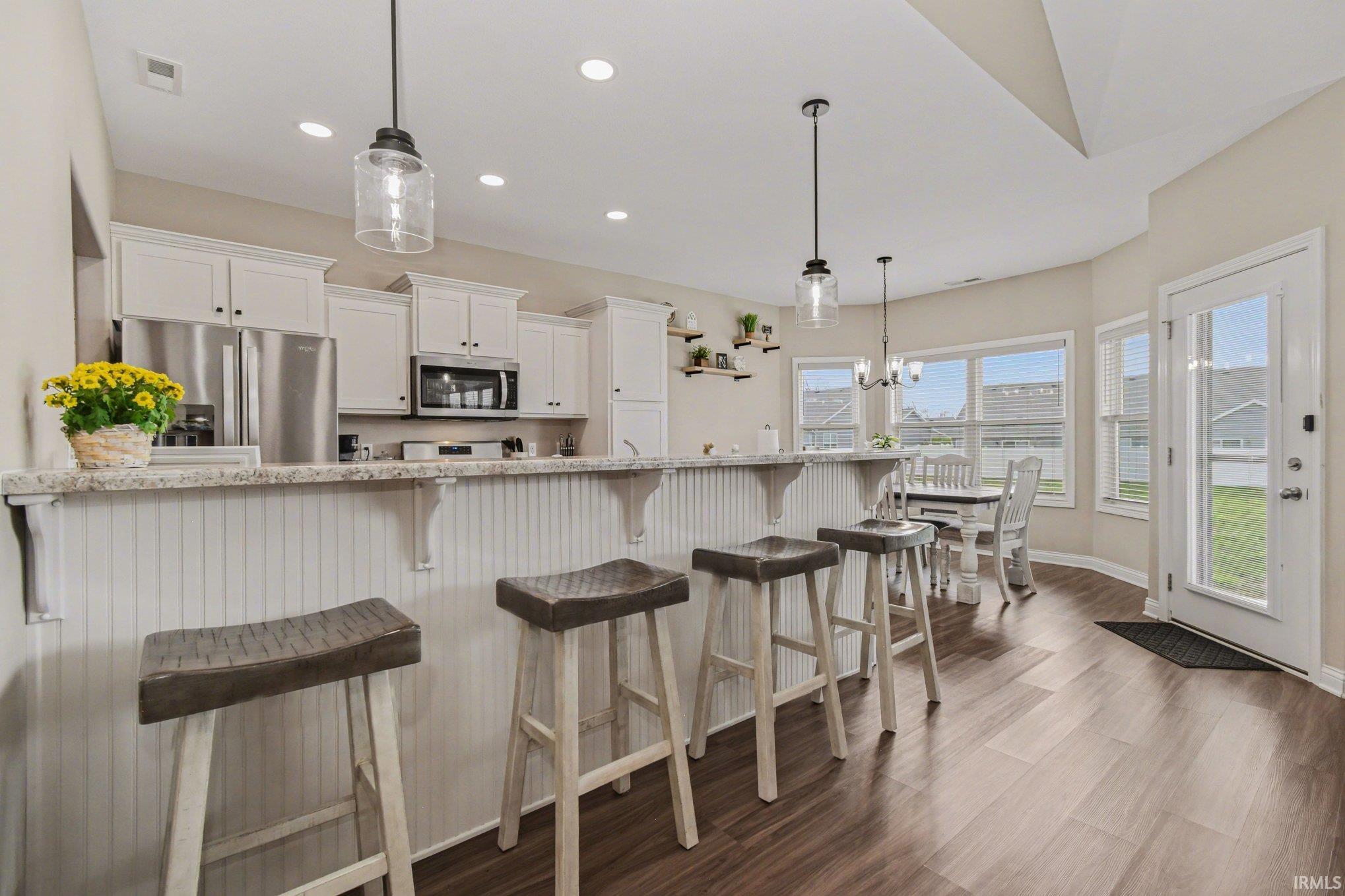 Kitchen featuring stainless steel appliances, white cabinets, a kitchen bar, dark wood-type flooring, and decorative light fixtures