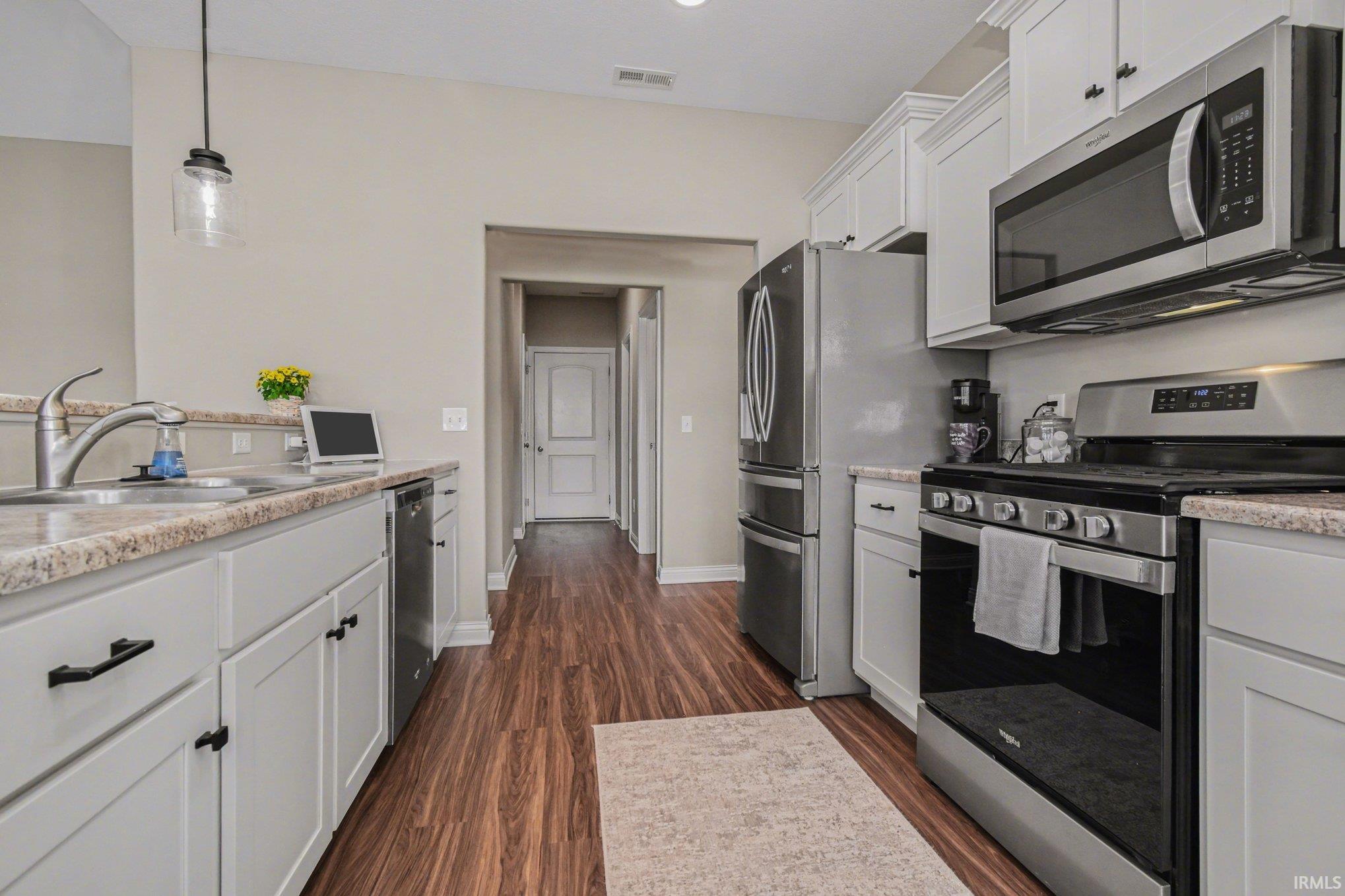 Kitchen featuring stainless steel appliances, dark wood finished floors, decorative light fixtures, and white cabinetry