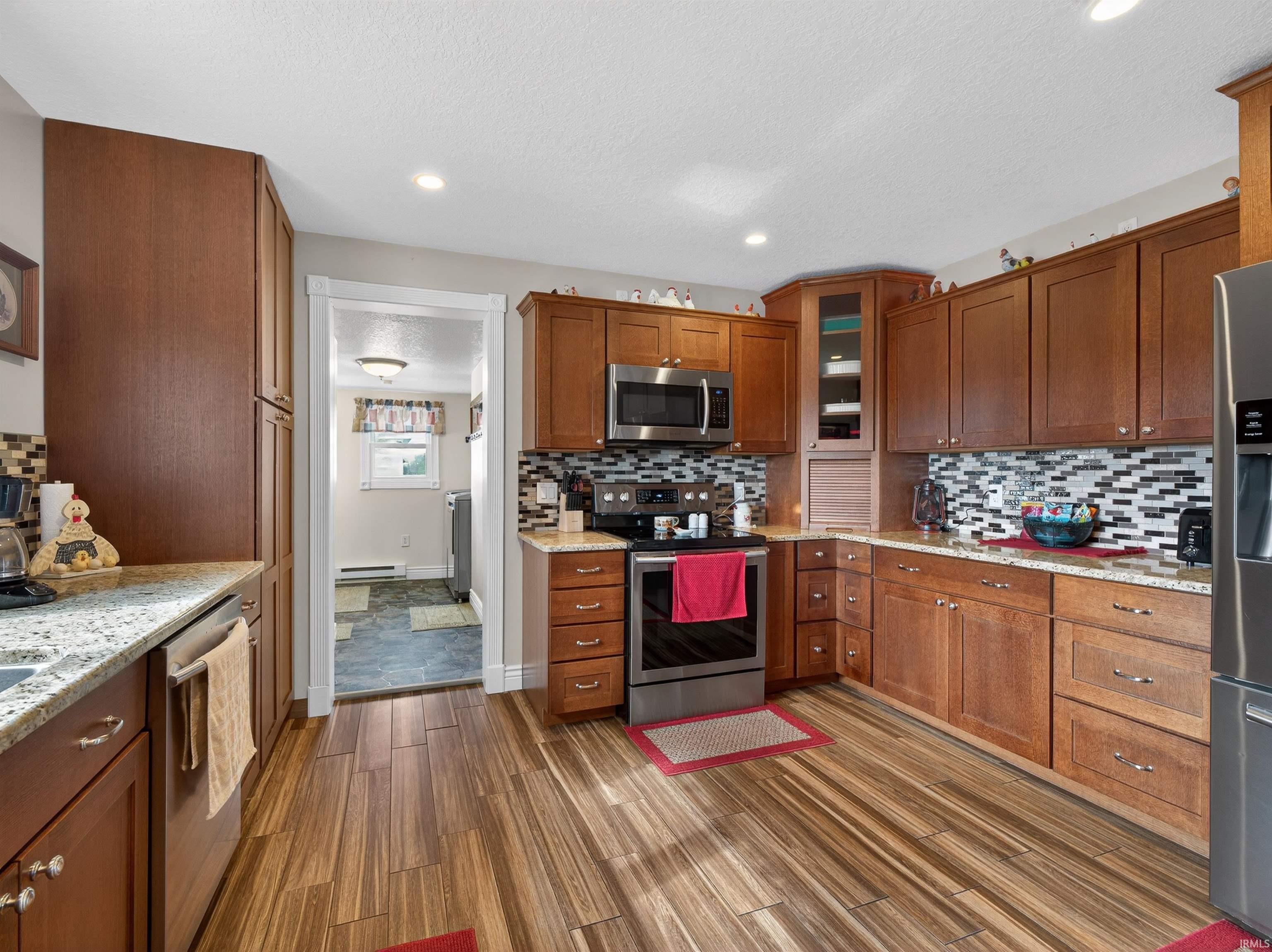 Kitchen featuring stainless steel appliances, glass fronted cabinets, wood finish cabinets, light stone counters, and recessed lighting