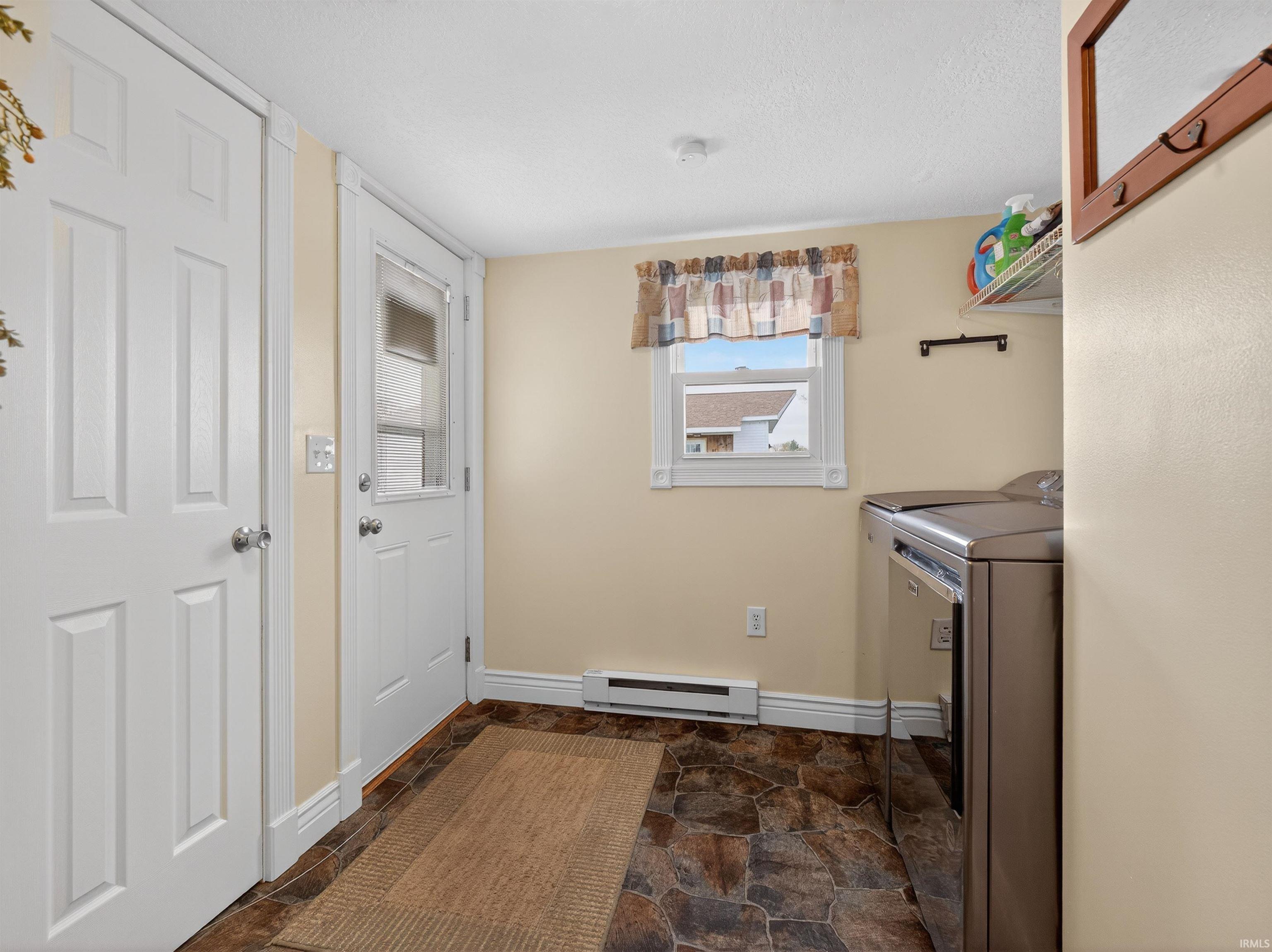 Laundry room featuring dark stone finish flooring, baseboard heating, and washer and clothes dryer