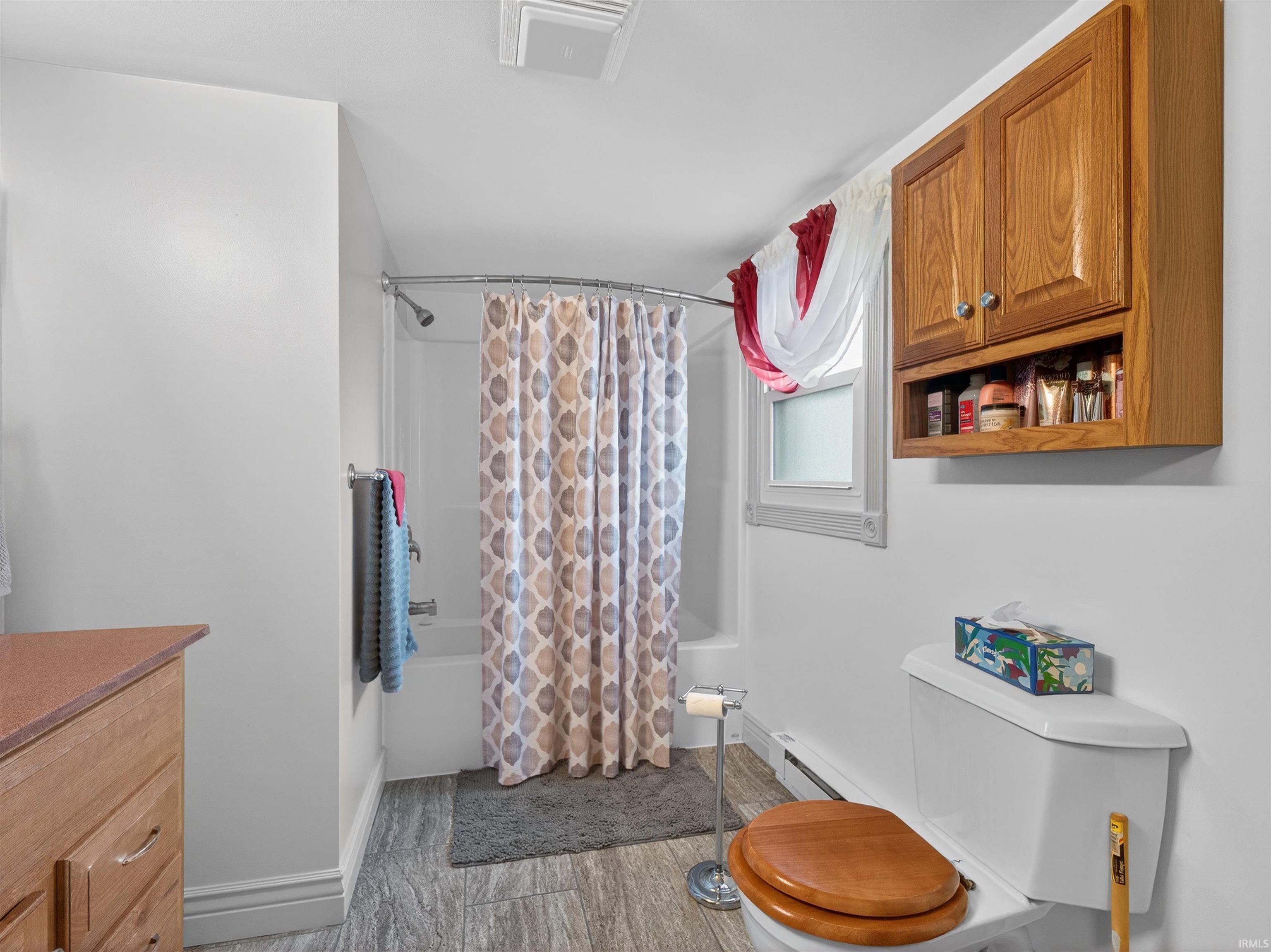 Bathroom with shower / tub combo with curtain, baseboard heating, vanity, and light wood-style floors