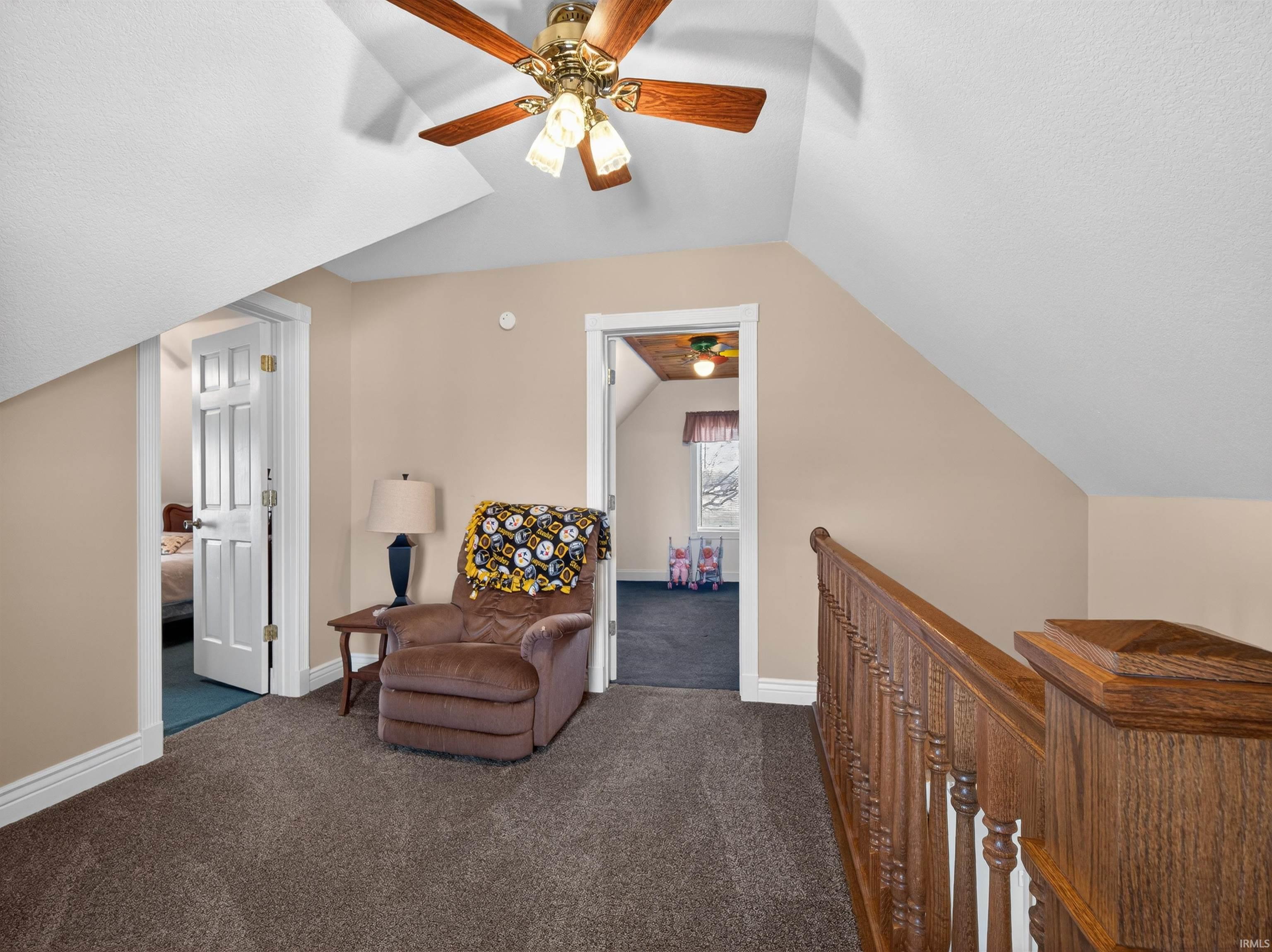 Living area featuring dark colored carpet, an upstairs landing, and a ceiling fan