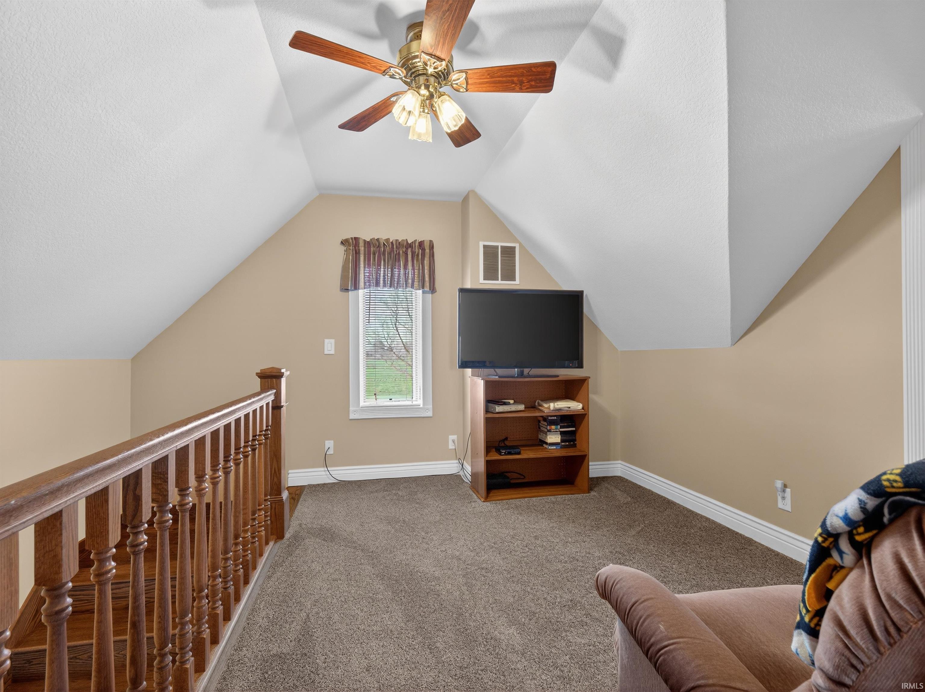 Living area with carpet flooring, a ceiling fan, and an upstairs landing